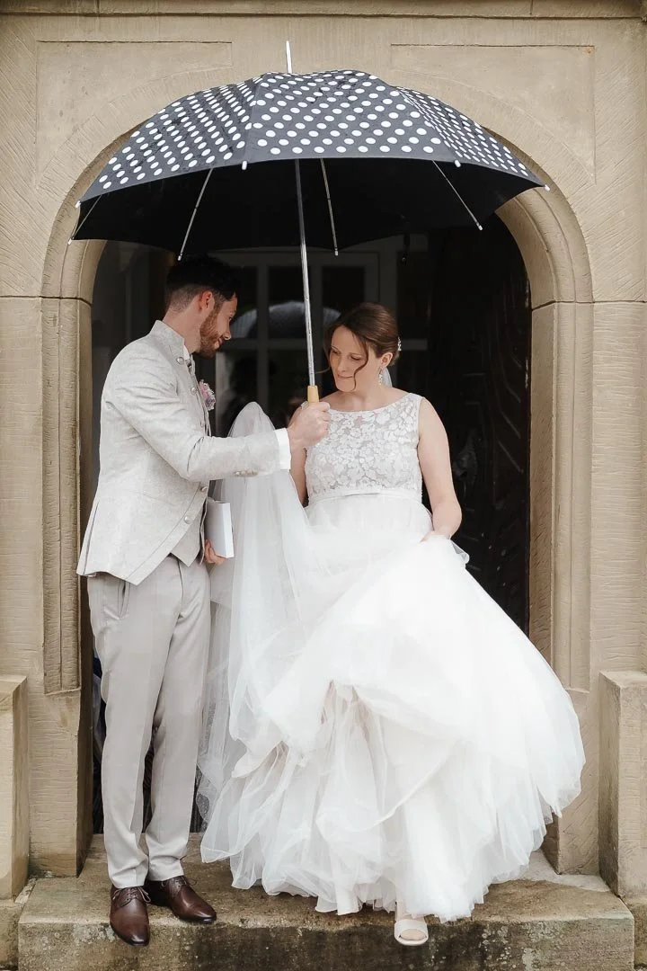 Hochzeitsfoto eines Brautpaares nach der Trauung vor dem Schloss Neuburg an der Kammel mit einem Regenschirm