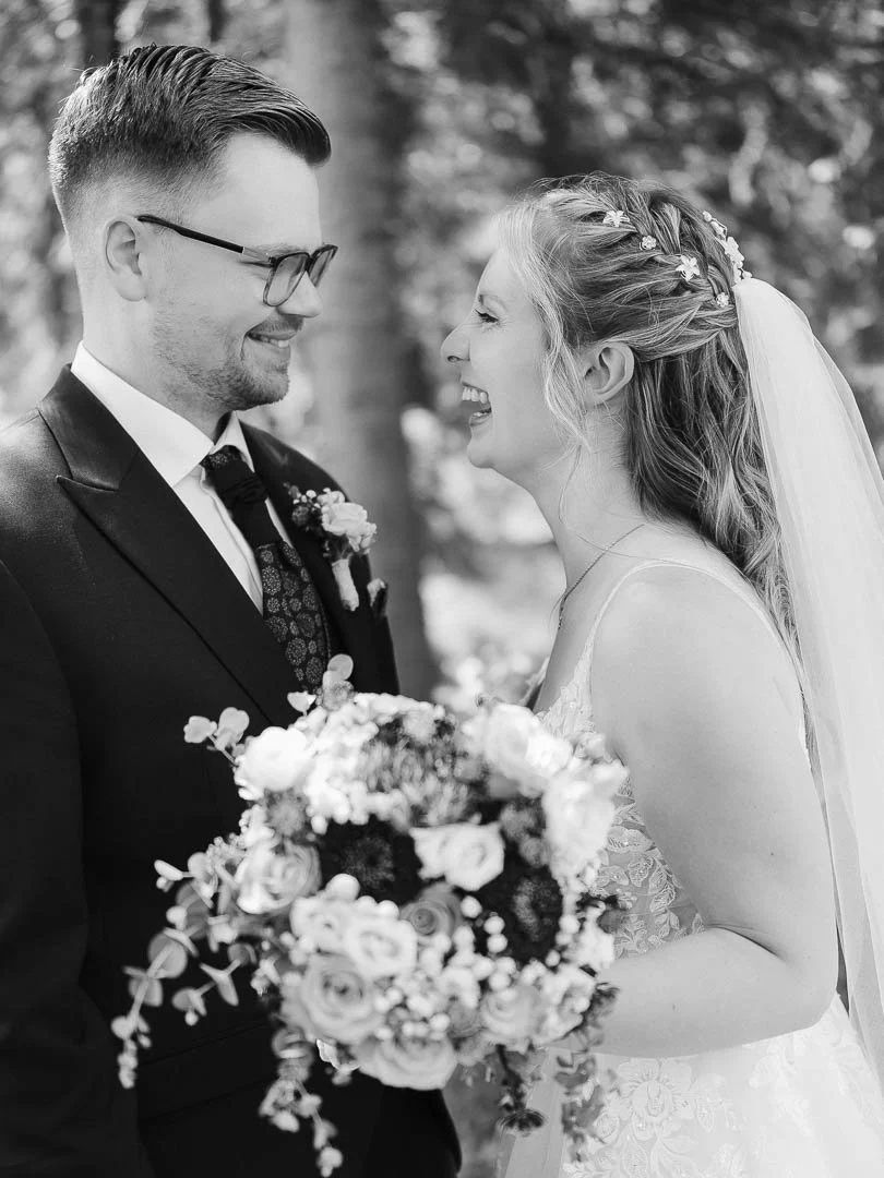 natürliches Schwarz-Weiß-Porträt eines lachendes Hochzeitspaares mit Brautstrauß