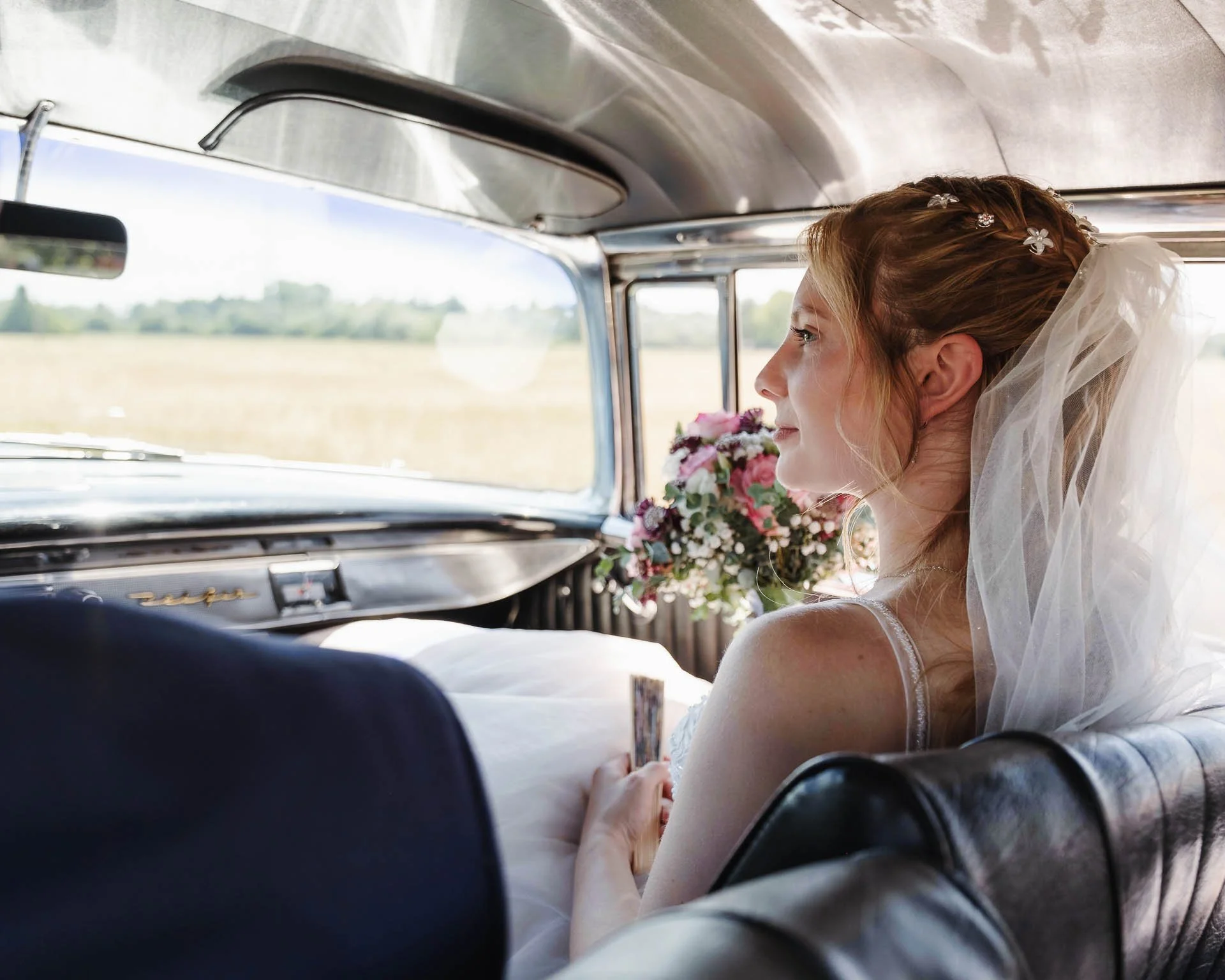 Eine Braut sitzt als Beifahrerin in einem Oldtimer und hält ihren Brautstrauss in der Hand 