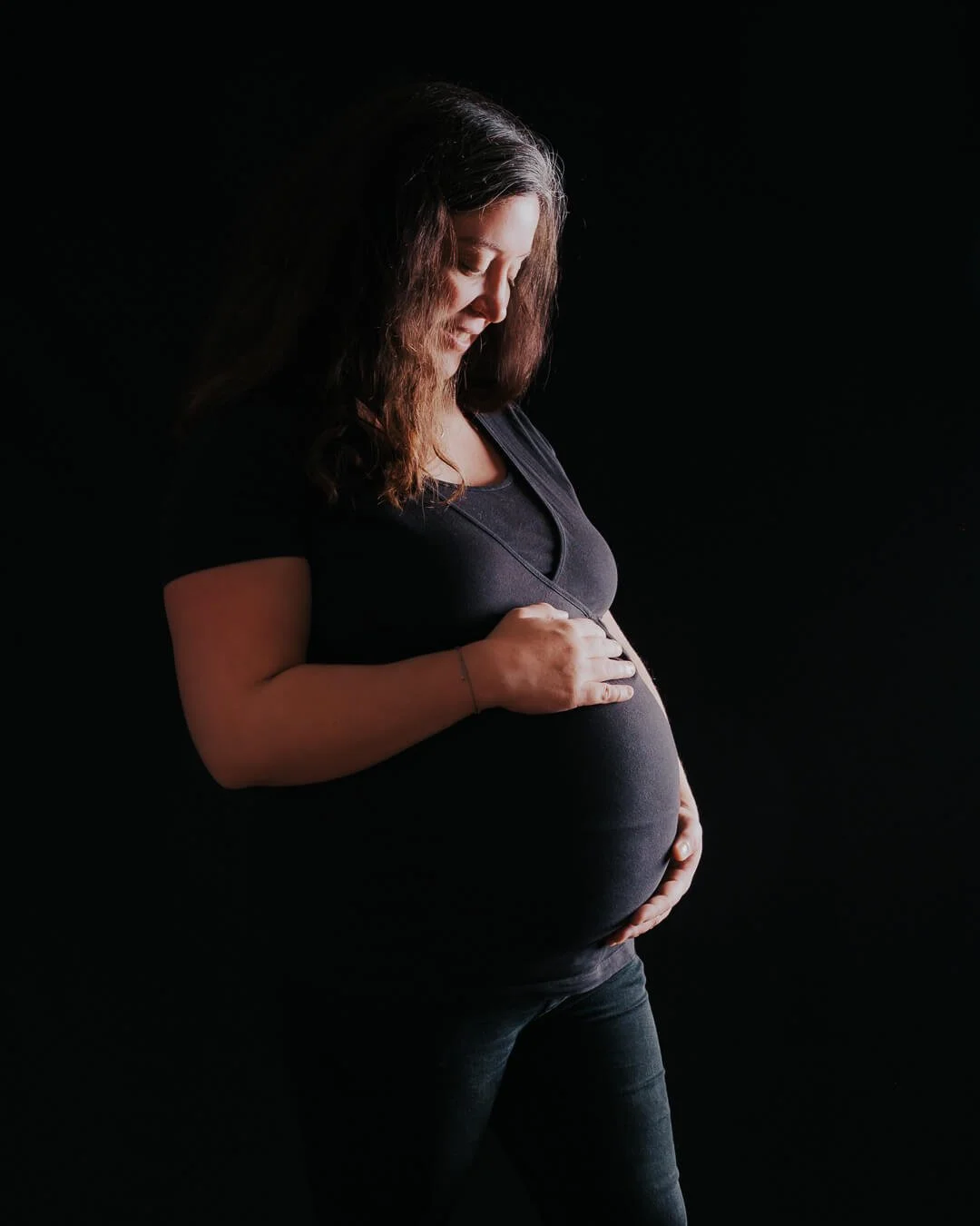 Schwangere Frau beim Babybauch-Fotoshooting im Fotostudio bei Augsburg mit schwarzem Hintergrund