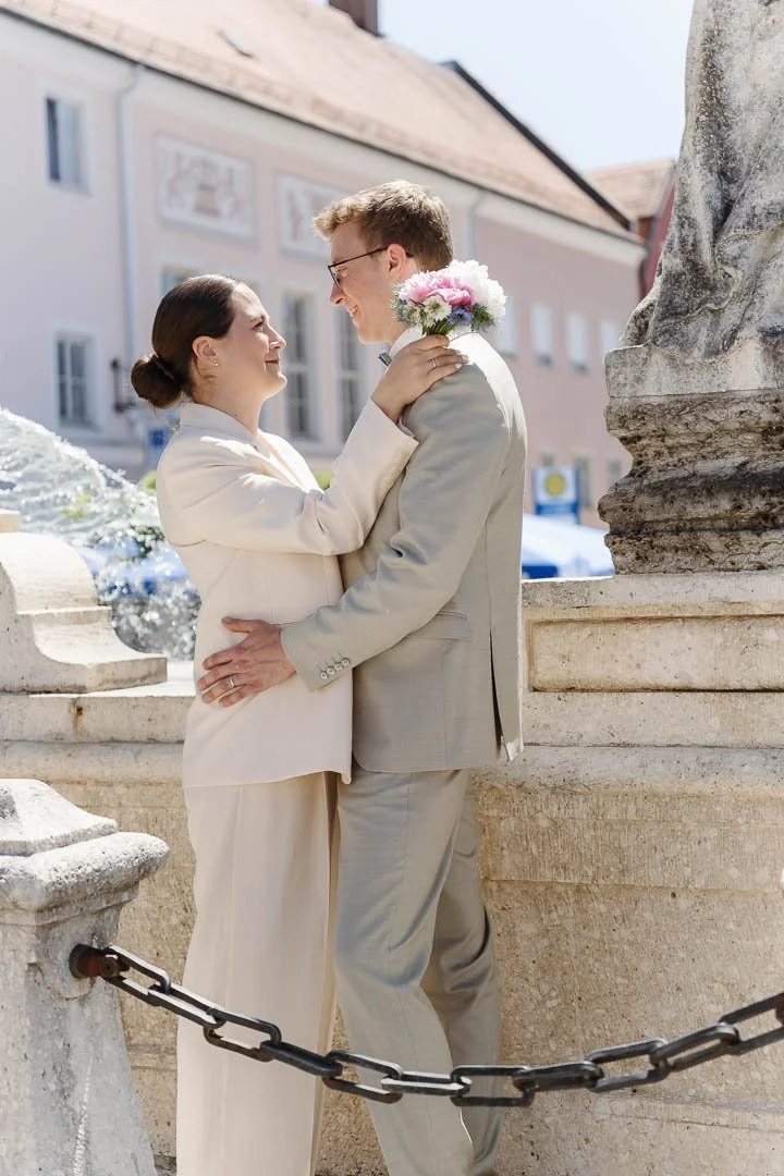 Ein Hochzeitspaar umarmt sich vor dem Brunnen neben dem Rathaus Friedberg und sieht sich liebevoll in die Augen