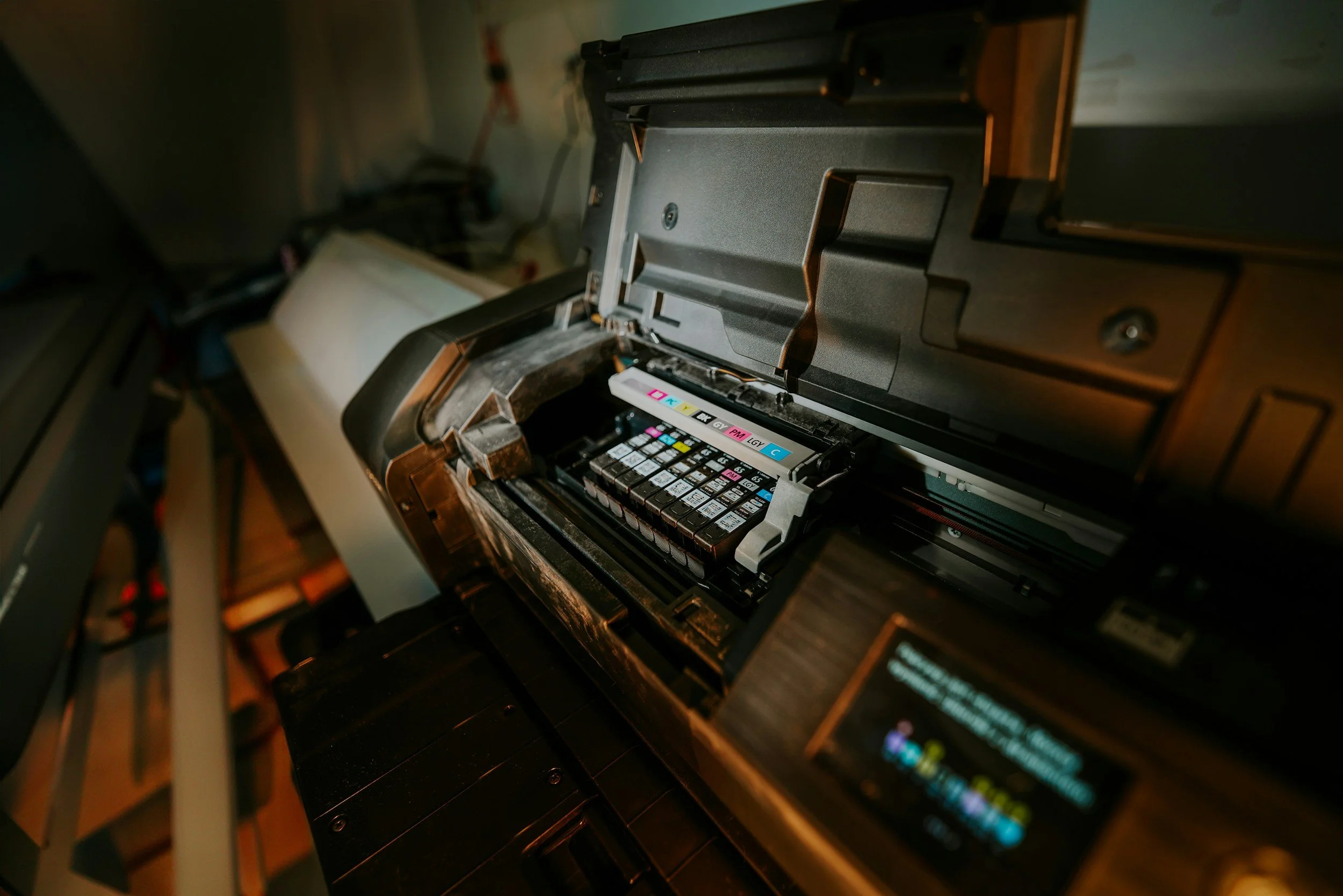 Printing Services. Close-up of a printer with its cover open, exposing the ink cartridges inside. The printer is on a black surface with a blurred background.