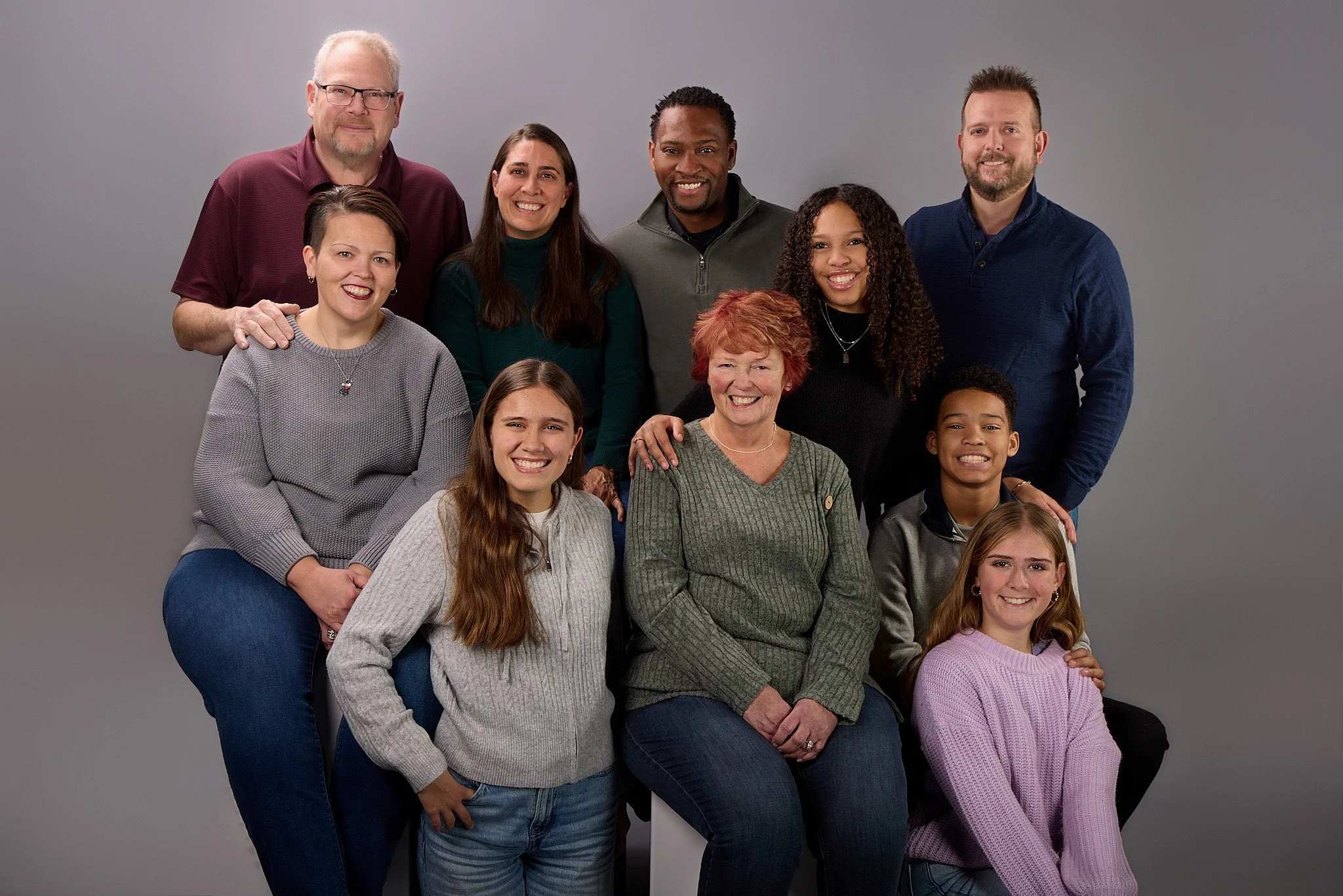 Family Picture - Group of ten people, including adults and children, sitting and standing against a gray background, smiling at the camera.