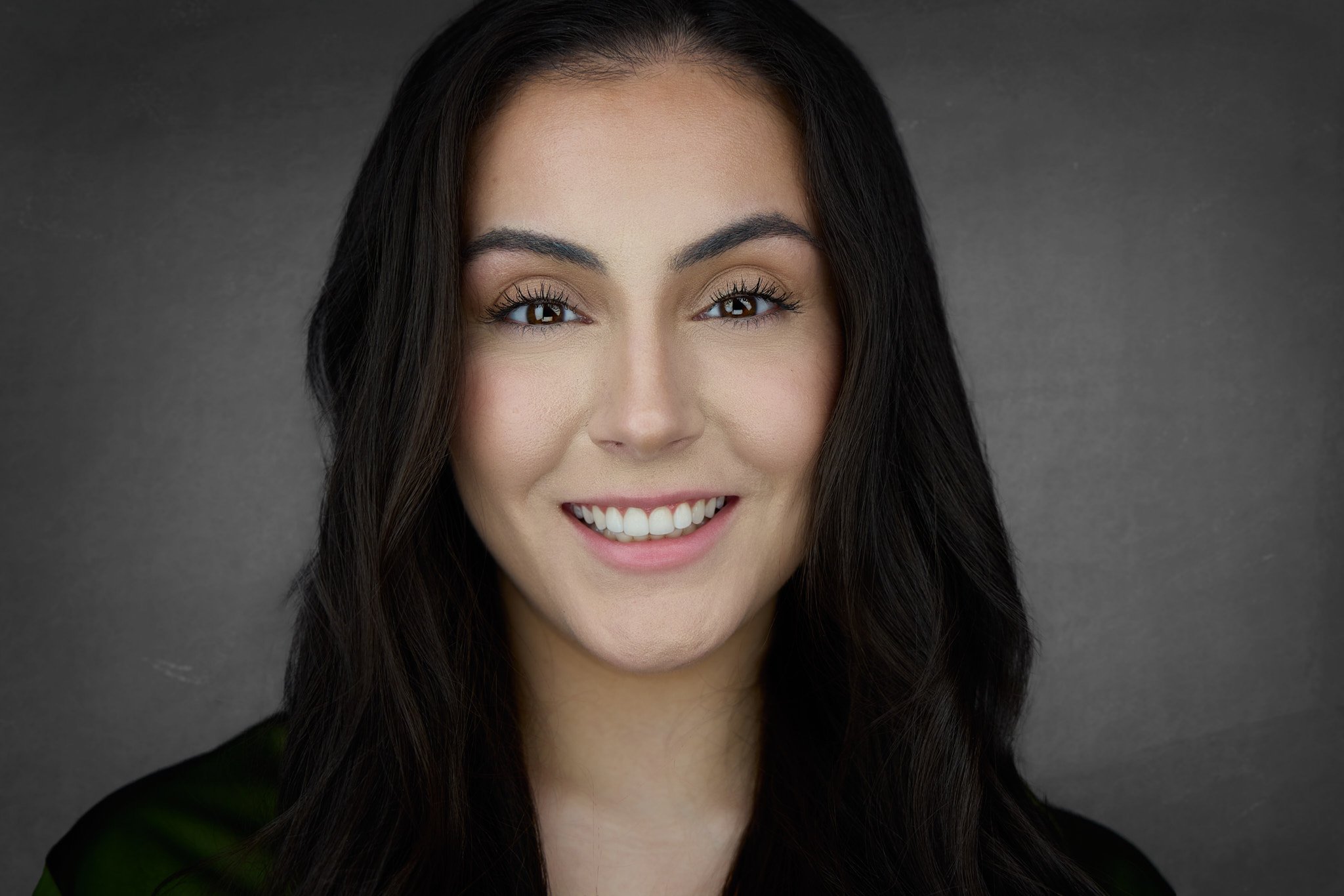 Close-up portrait of a woman with long dark hair, bright smile, brown eyes, and wearing a dark top.