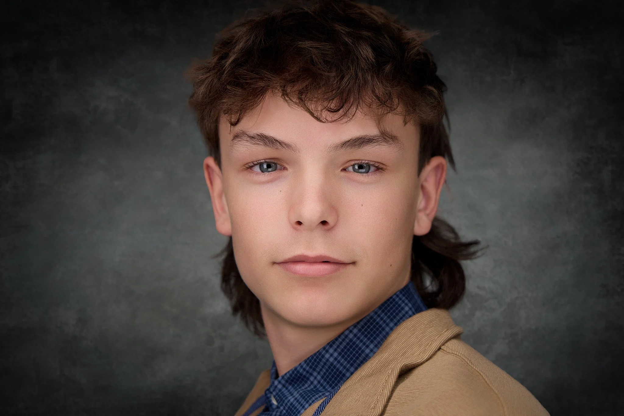 Headshot- young man brown jacket mullet headshot