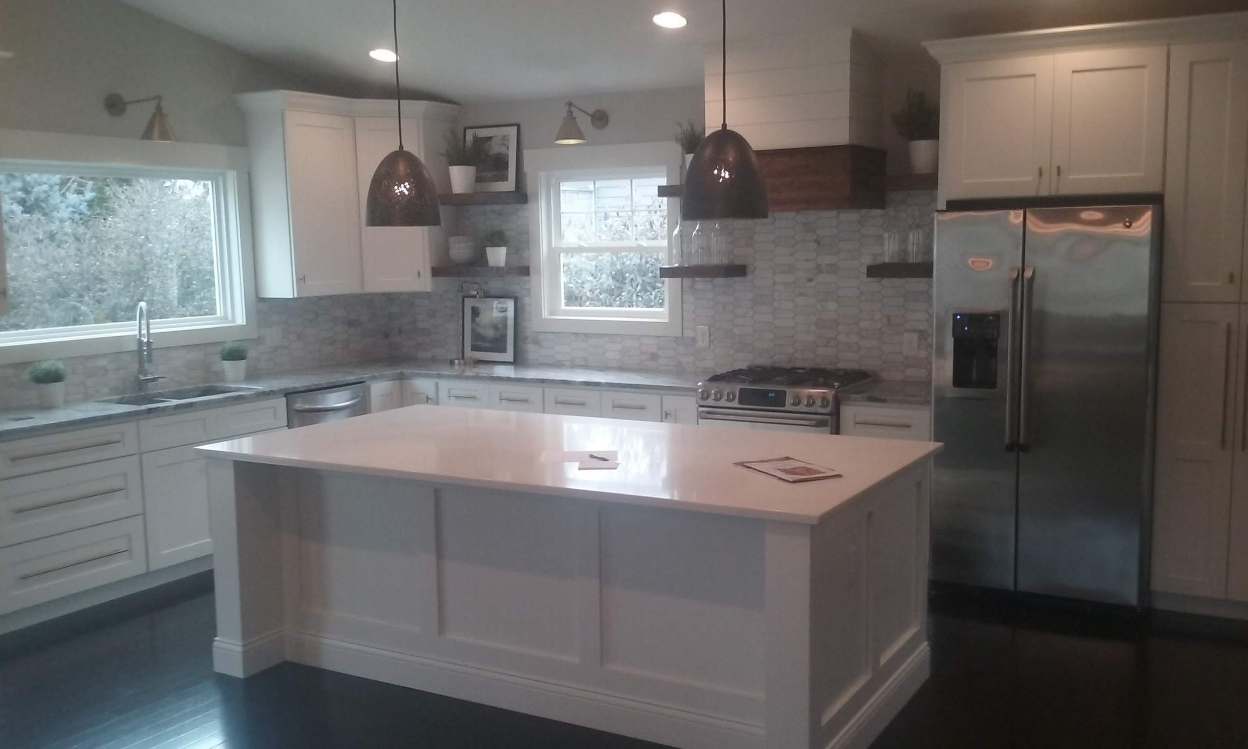 Modern kitchen with white cabinets, a central island, stainless steel appliances, and a window overhead sink.