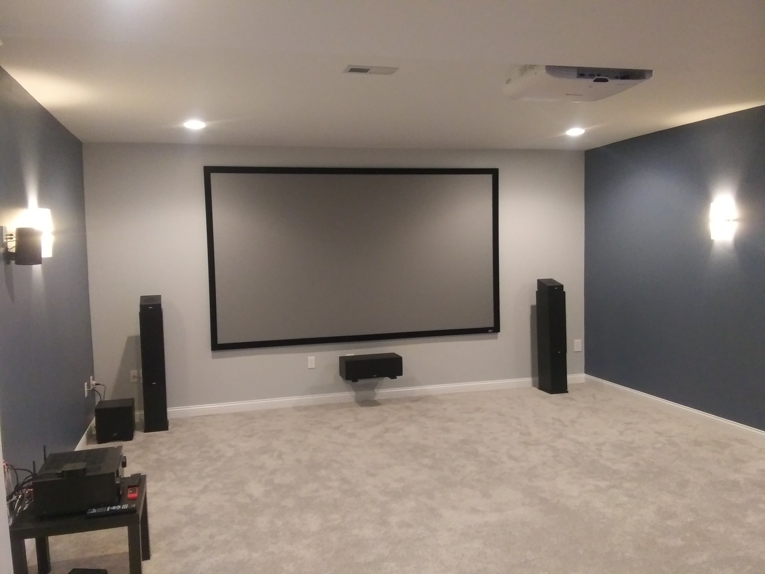 A home theater room with a large projection screen, surround sound speakers, and wall sconces for lighting.