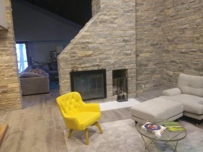 Living room with stone fireplace, yellow armchair, gray sectional sofa, and glass coffee table.