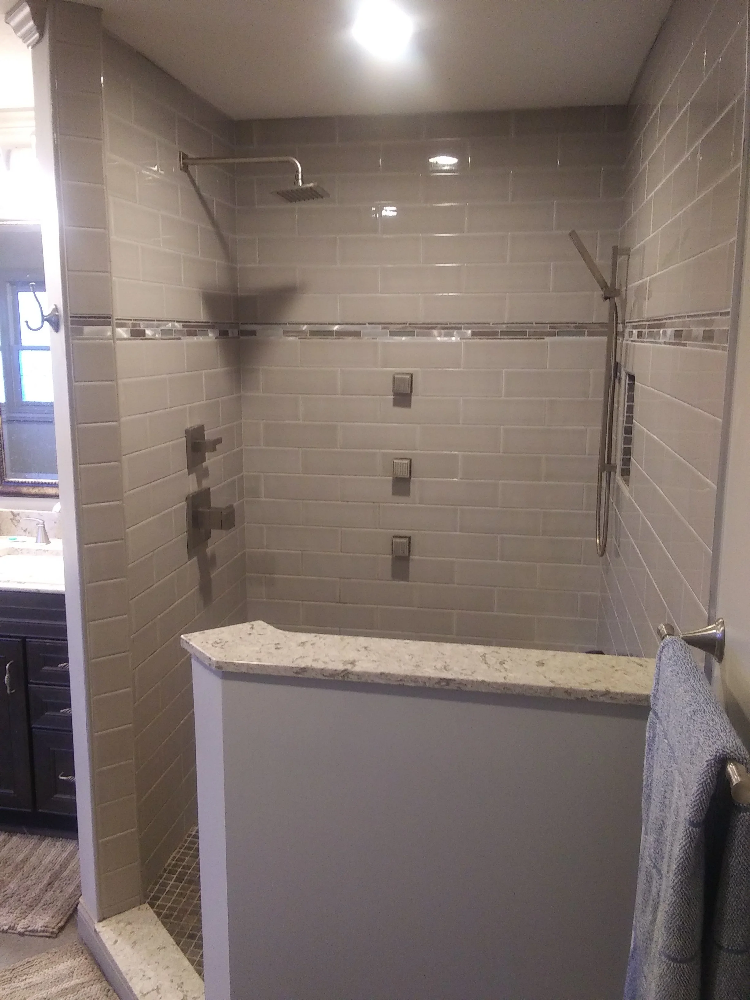 A bathroom shower with beige subway tiles, diverging showerheads, and a partial view of bathroom accessories on the right.