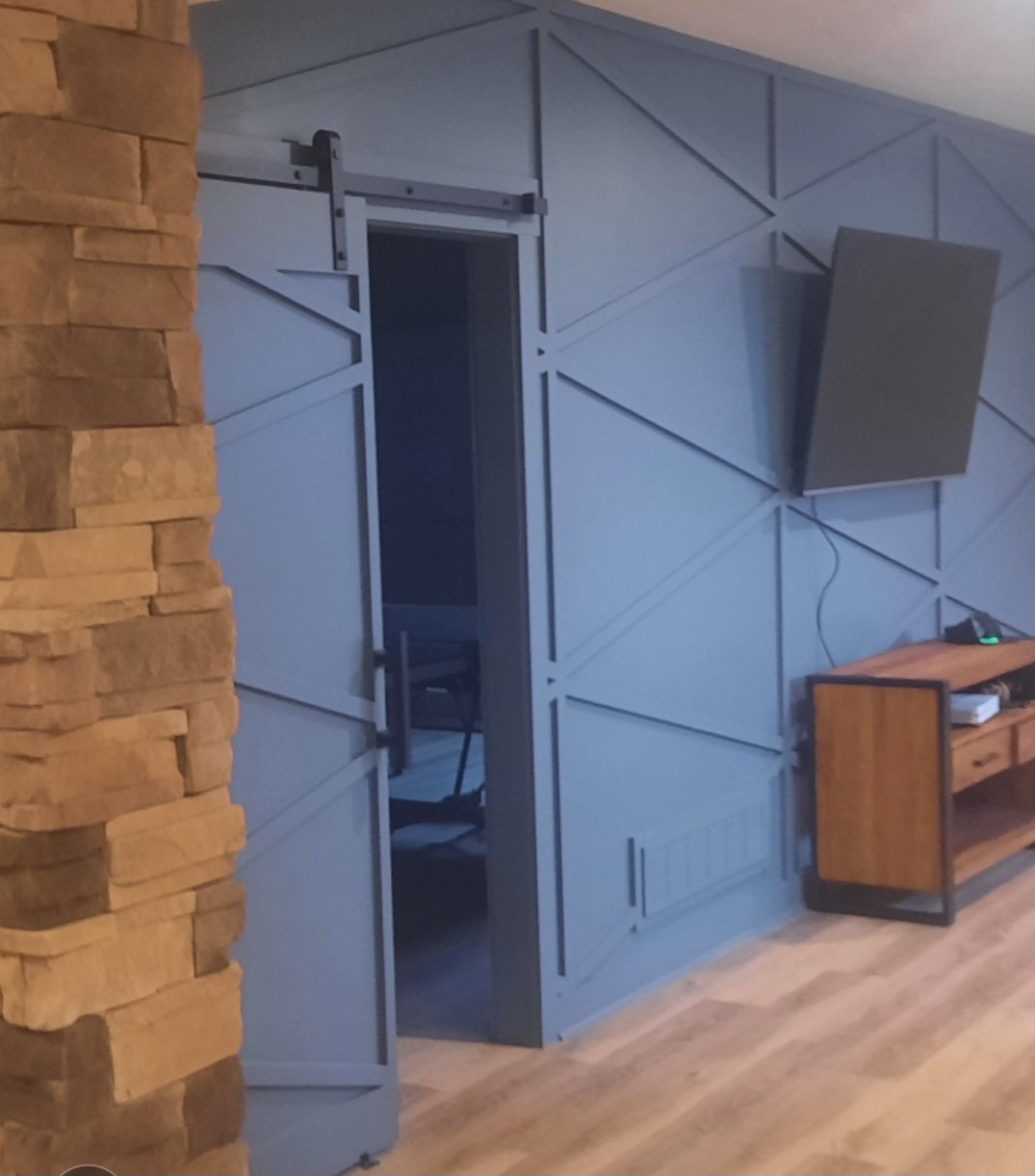 Interior home decor featuring a stone wall on the left, a blue sliding barn door, and a wooden console table with electronic devices.