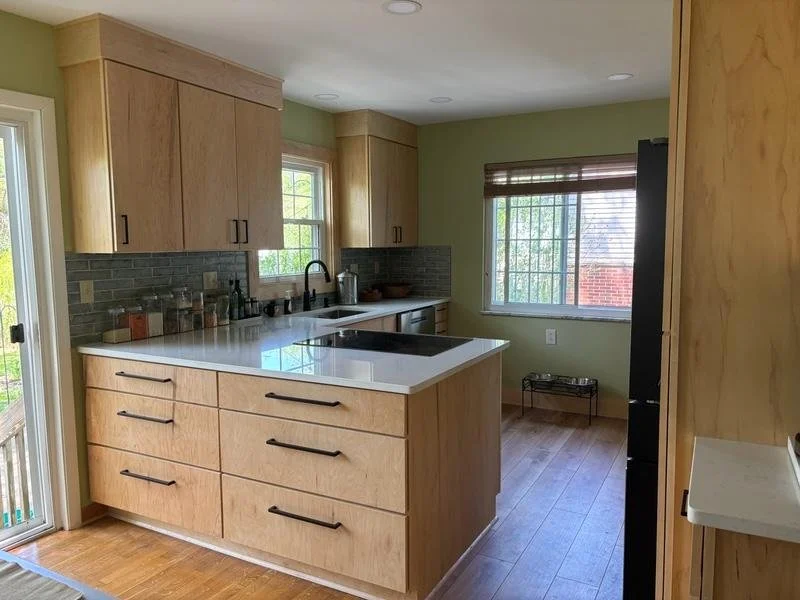 Kitchen with wooden cabinets, a white countertop, black handles, a window with blinds, and a stove in a well-lit room.