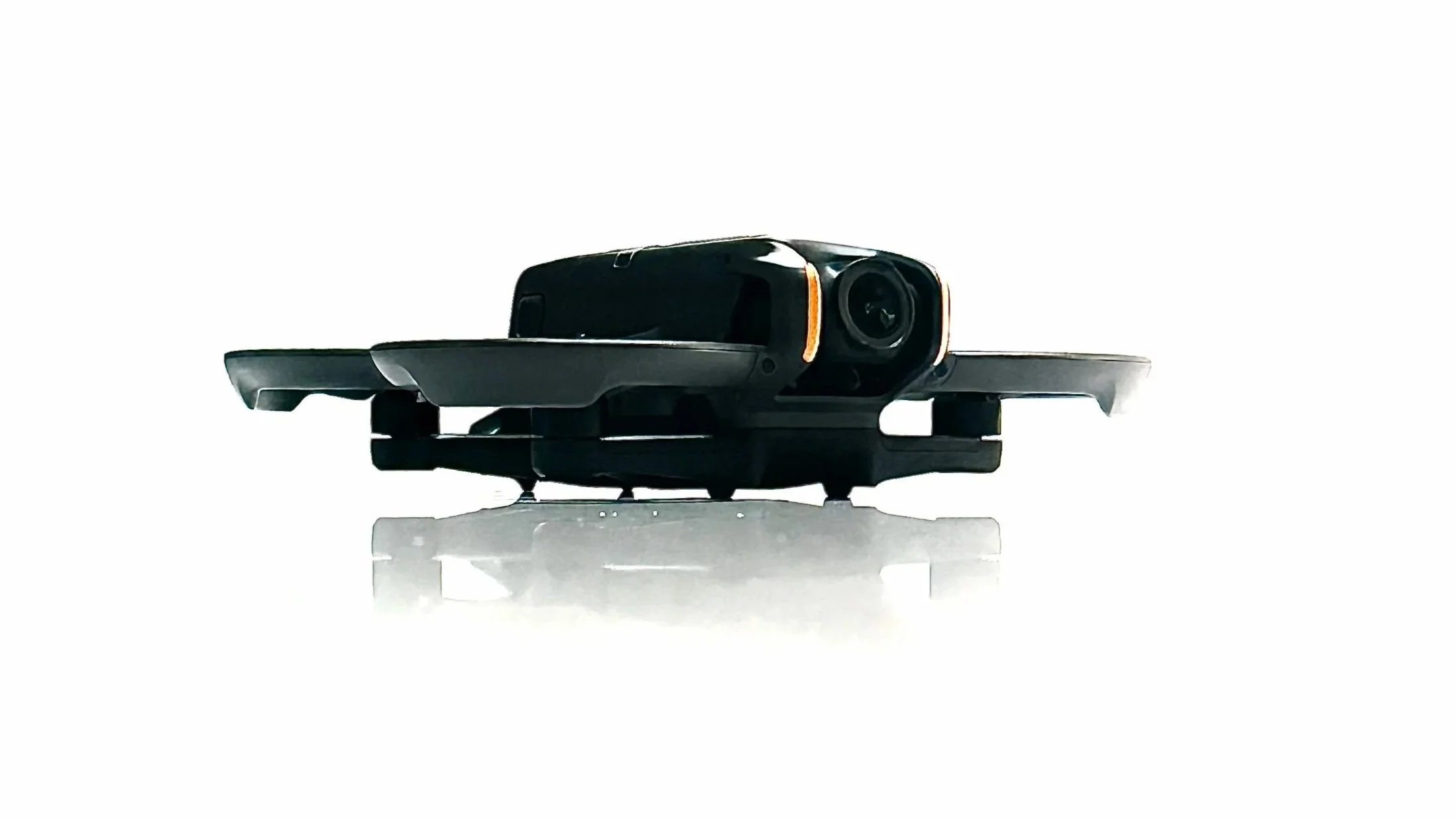 Close-up of a black drone with a camera, isolated on a white background, with a reflective surface below.