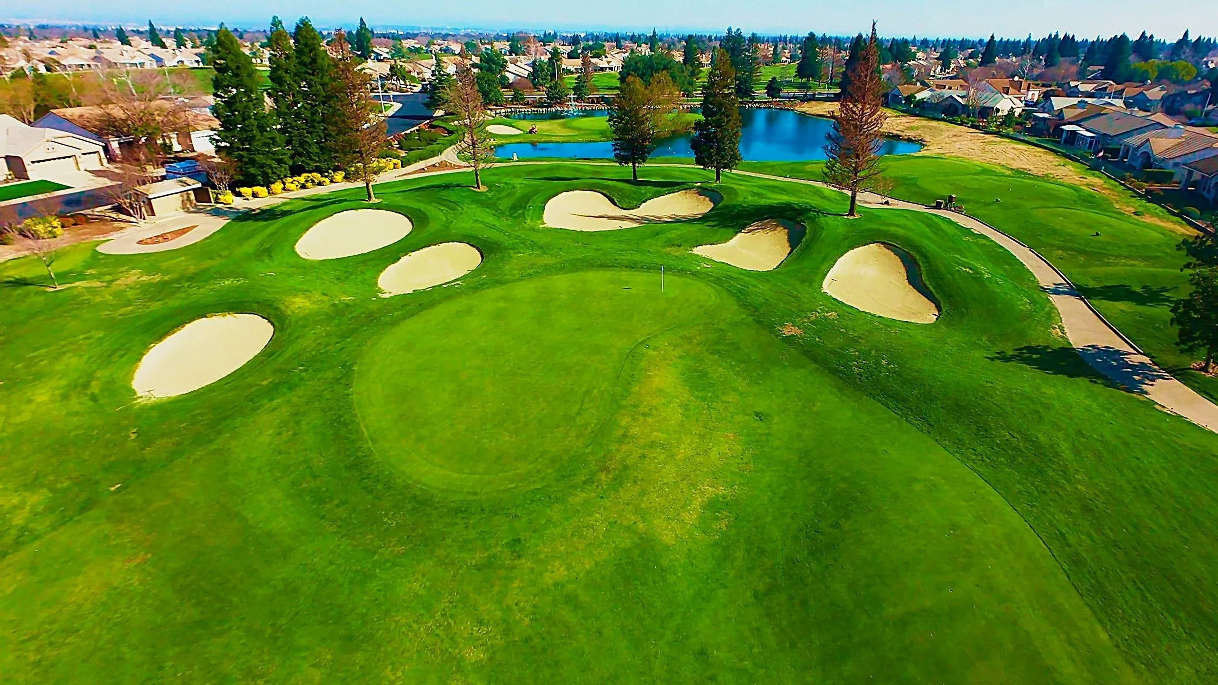 Aerial view of a golf course with sand bunkers, a pond, and surrounding neighborhood homes.