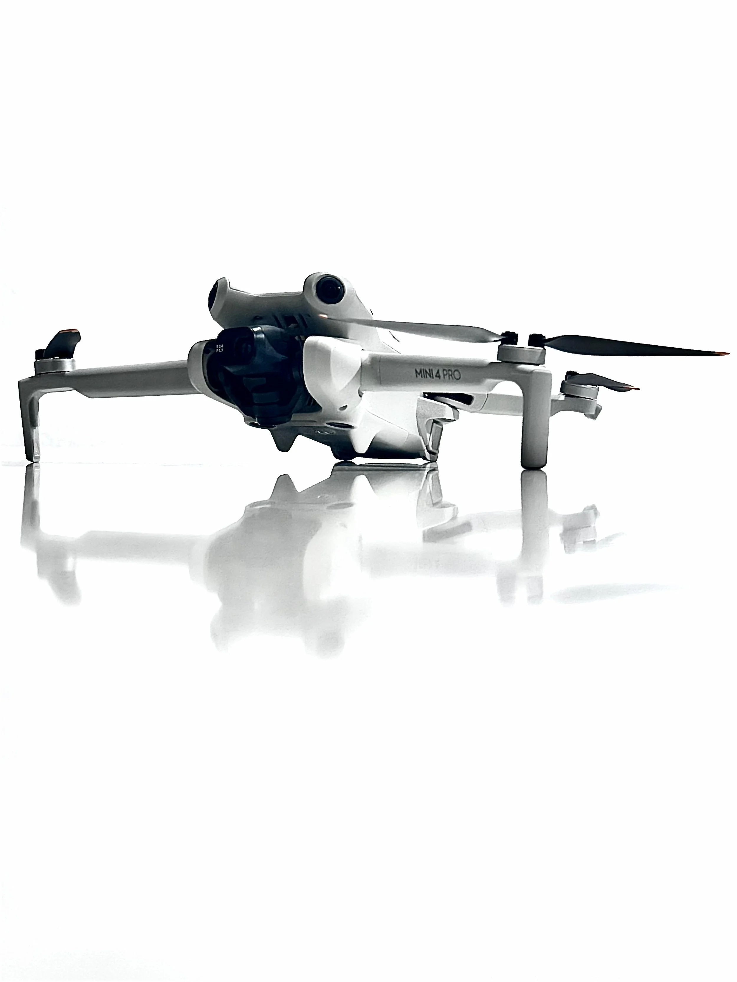 A white drone with four arms and propellers, labeled 'MINI 4 PRO,' resting on a reflective white surface with a plain white background.
