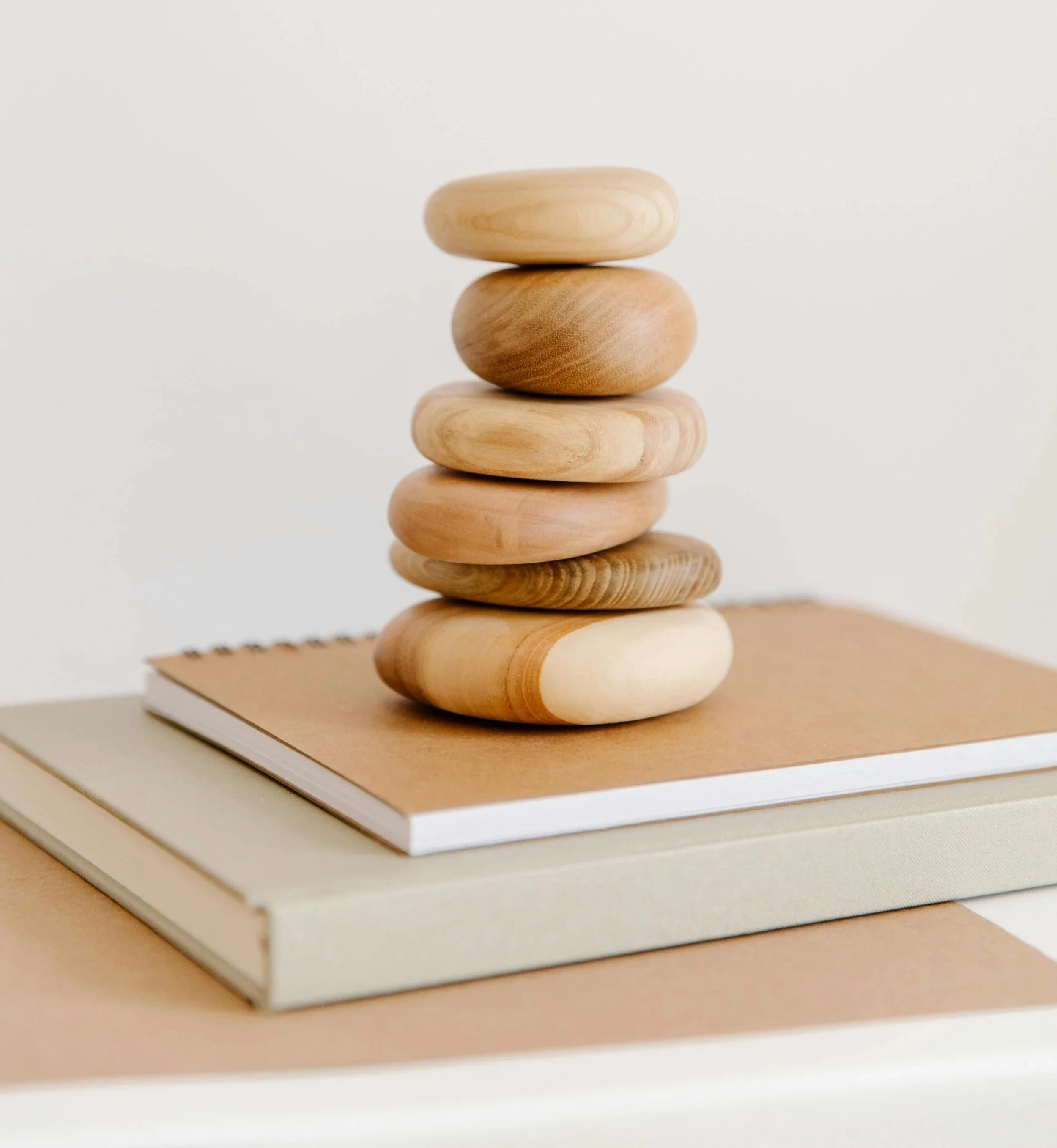 Stacked wooden stones on top of two closed books with neutral-colored covers, set against a white background.