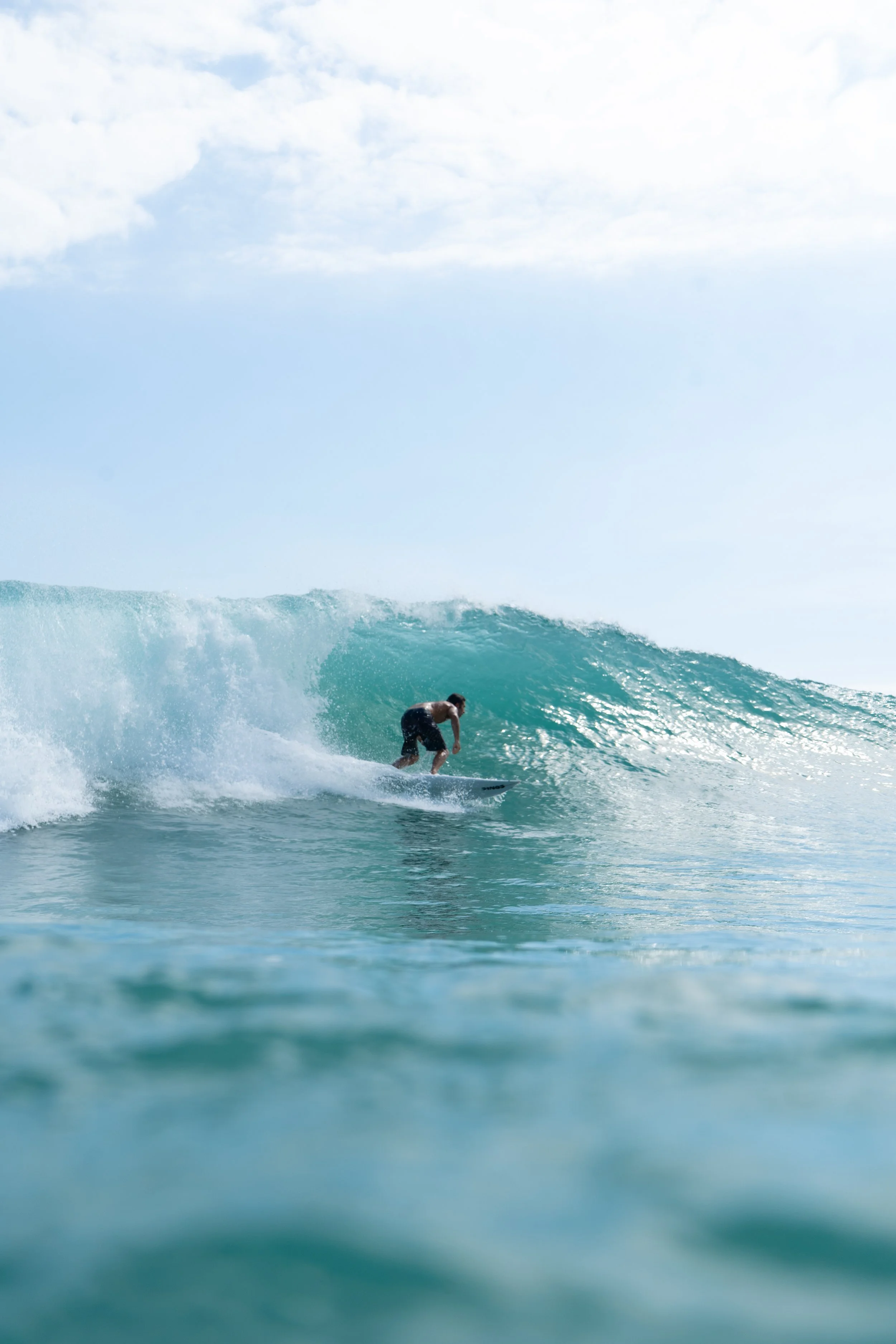 A person surfing on a wave in the ocean under a partly cloudy sky.