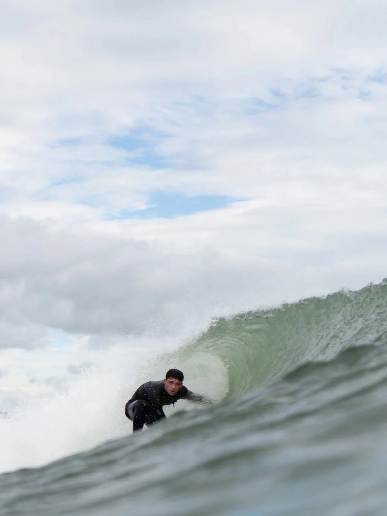 A person in a black wetsuit surfing inside a large wave in the ocean.