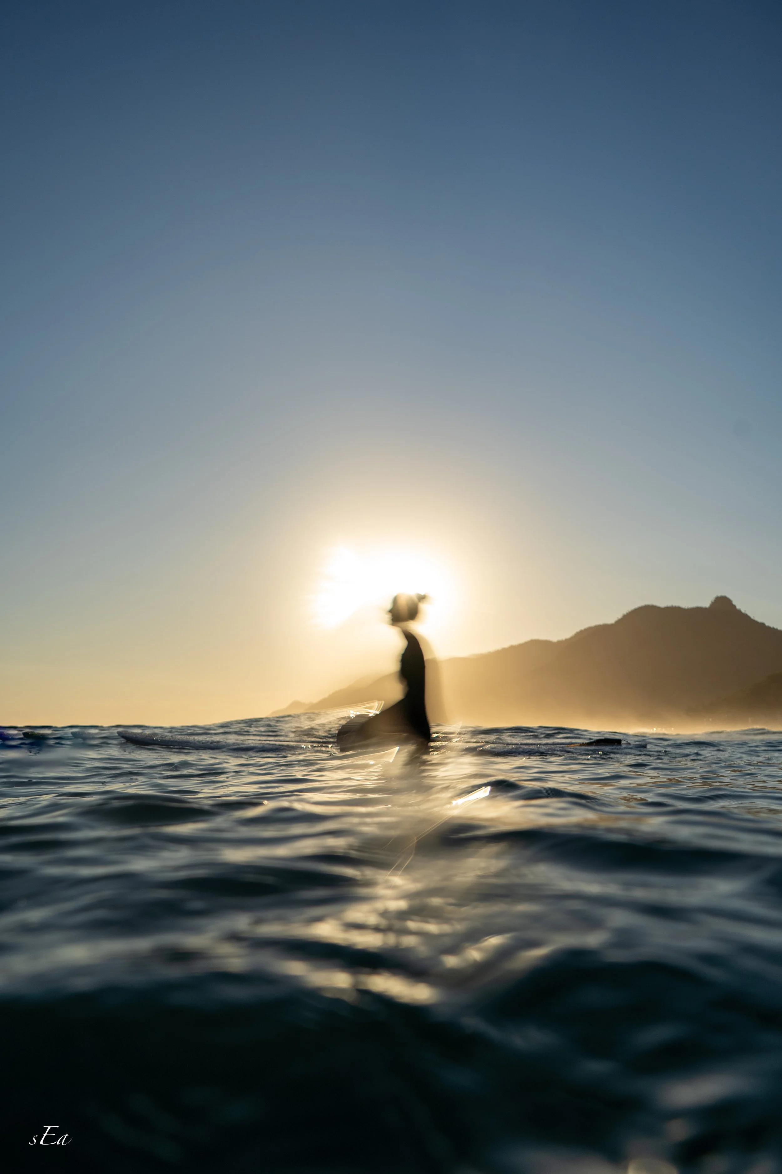 Person standing in the ocean at sunset with mountains in the background