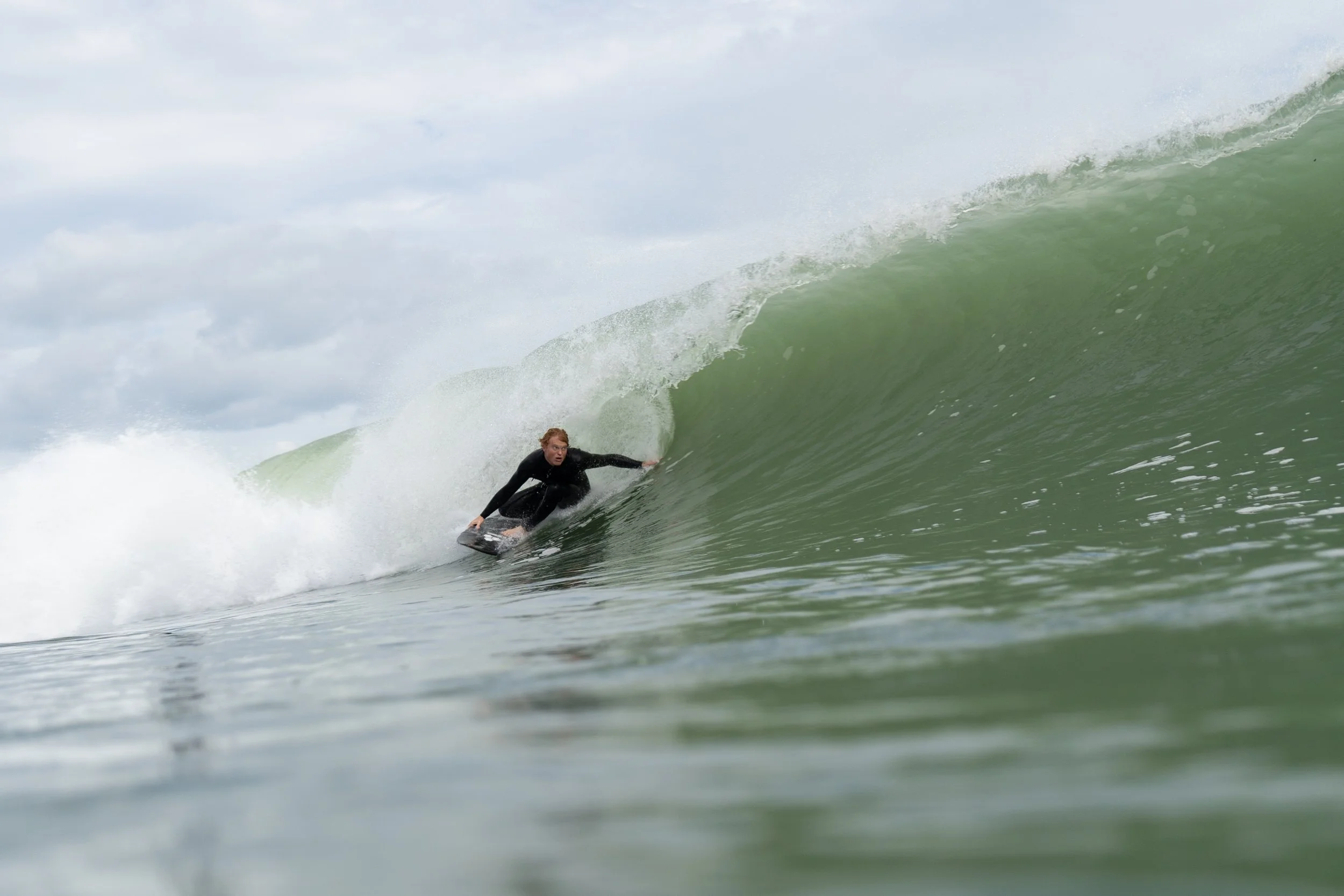 A person surfing on a green wave in the ocean with cloudy sky in the background.