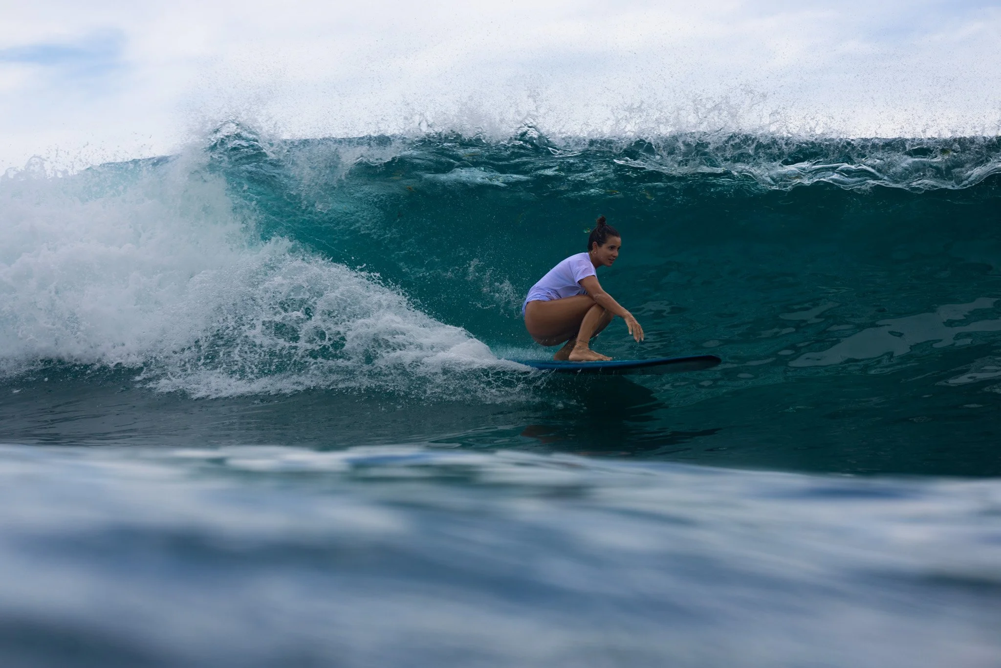 Woman surfing on a large ocean wave, crouched on her surfboard in a squatting position.