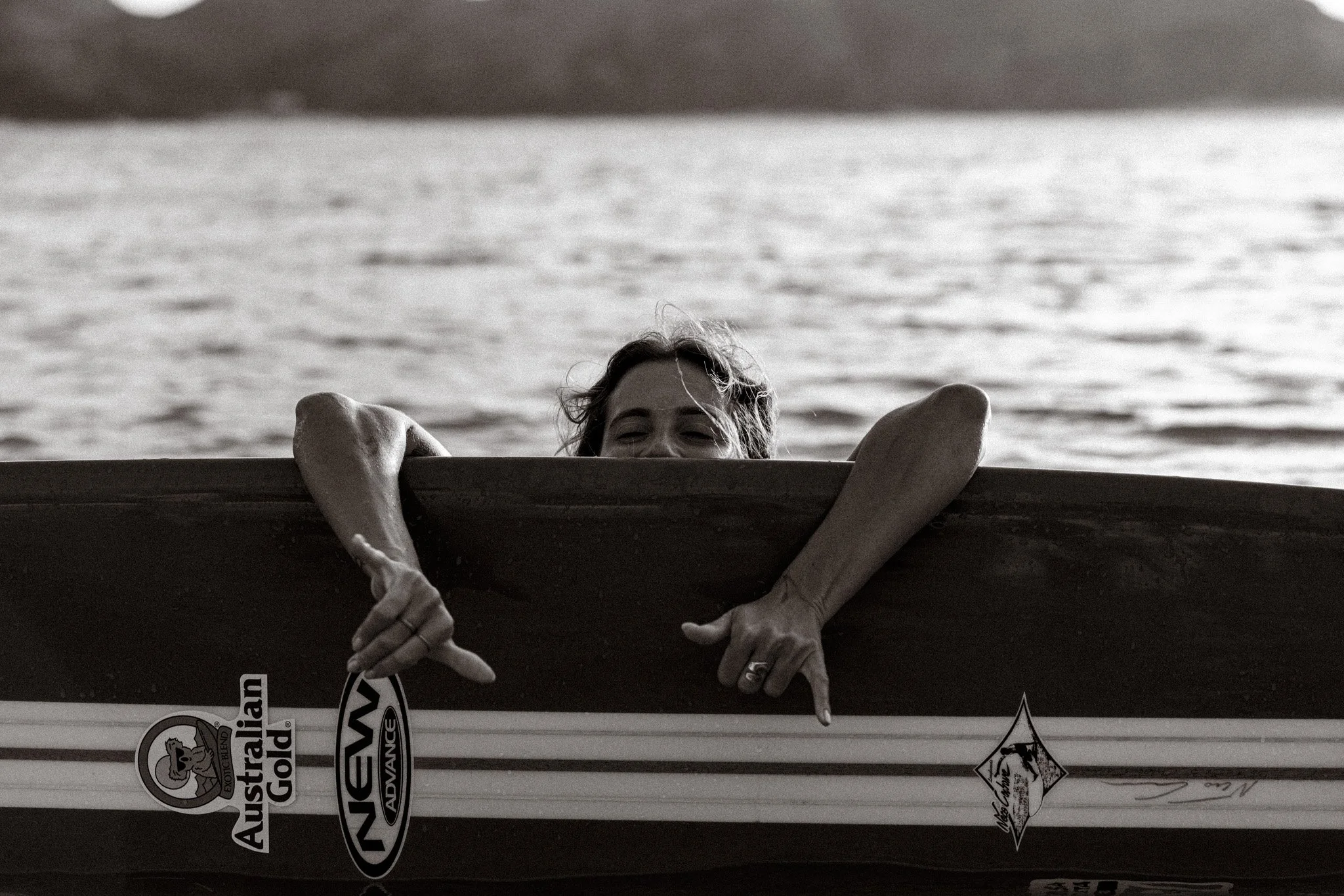 Person peeking over edge of a boat on a body of water, with arms resting on boat's side, black and white photograph