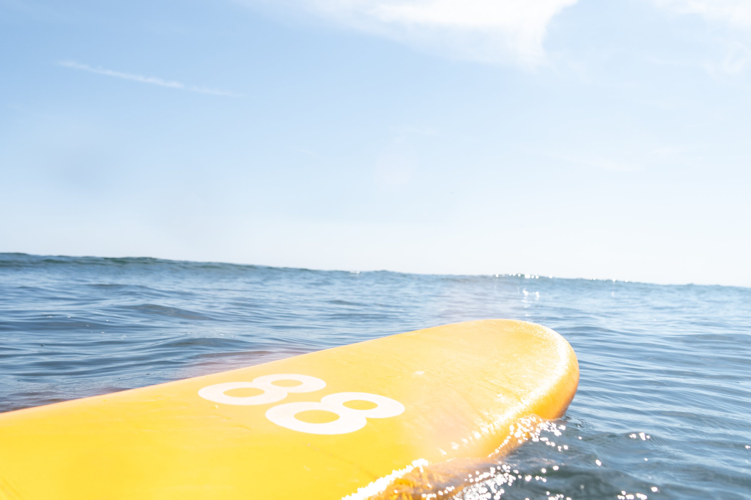 Close-up of a yellow surfboard with the number 68 printed on it, floating on the ocean water with a clear sky in the background.