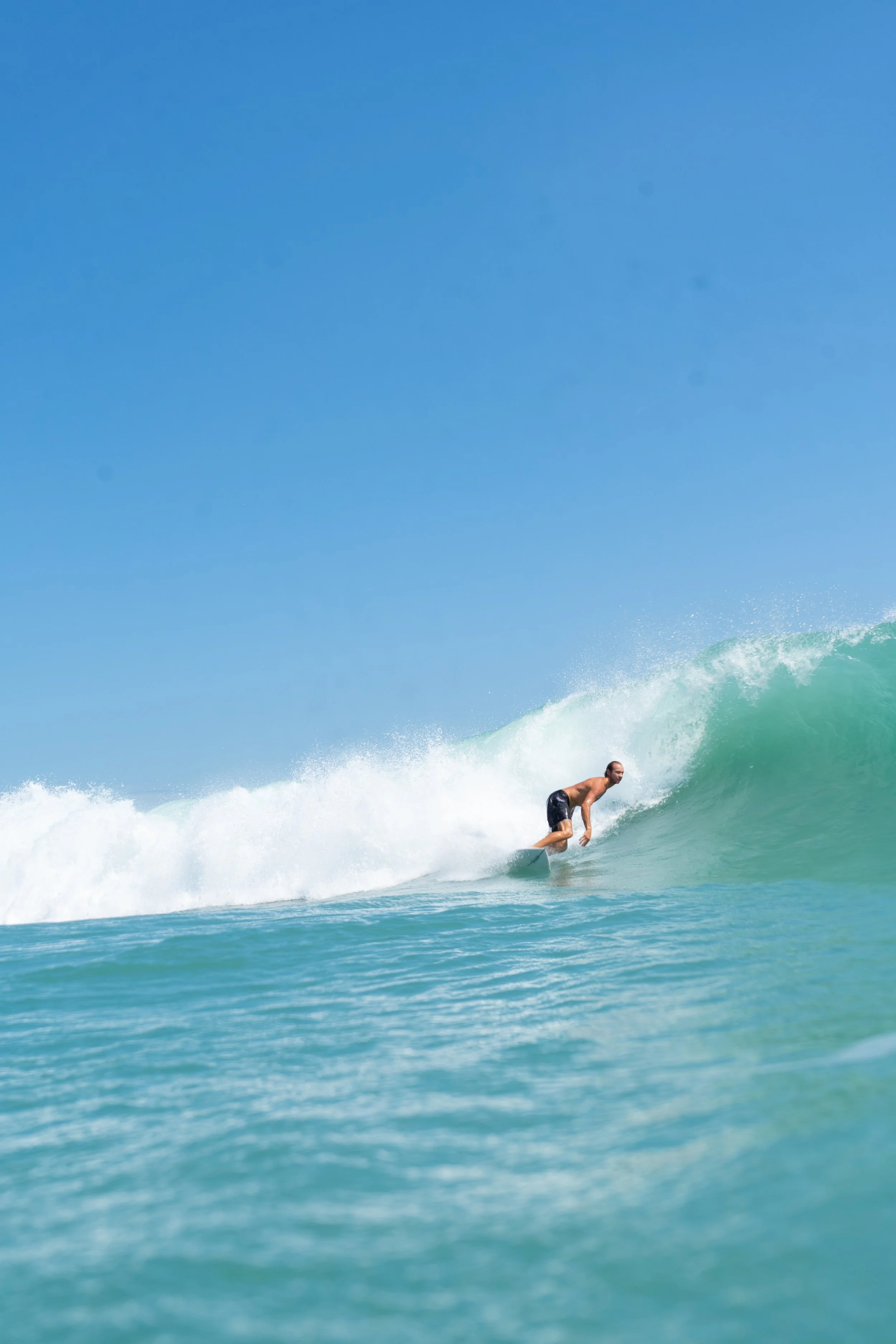 A man surfing on a wave at the beach with clear blue sky in the background.