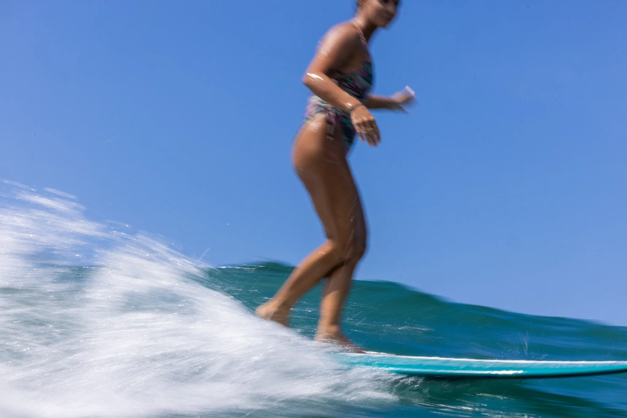 A person surfing on a wave under a clear blue sky.