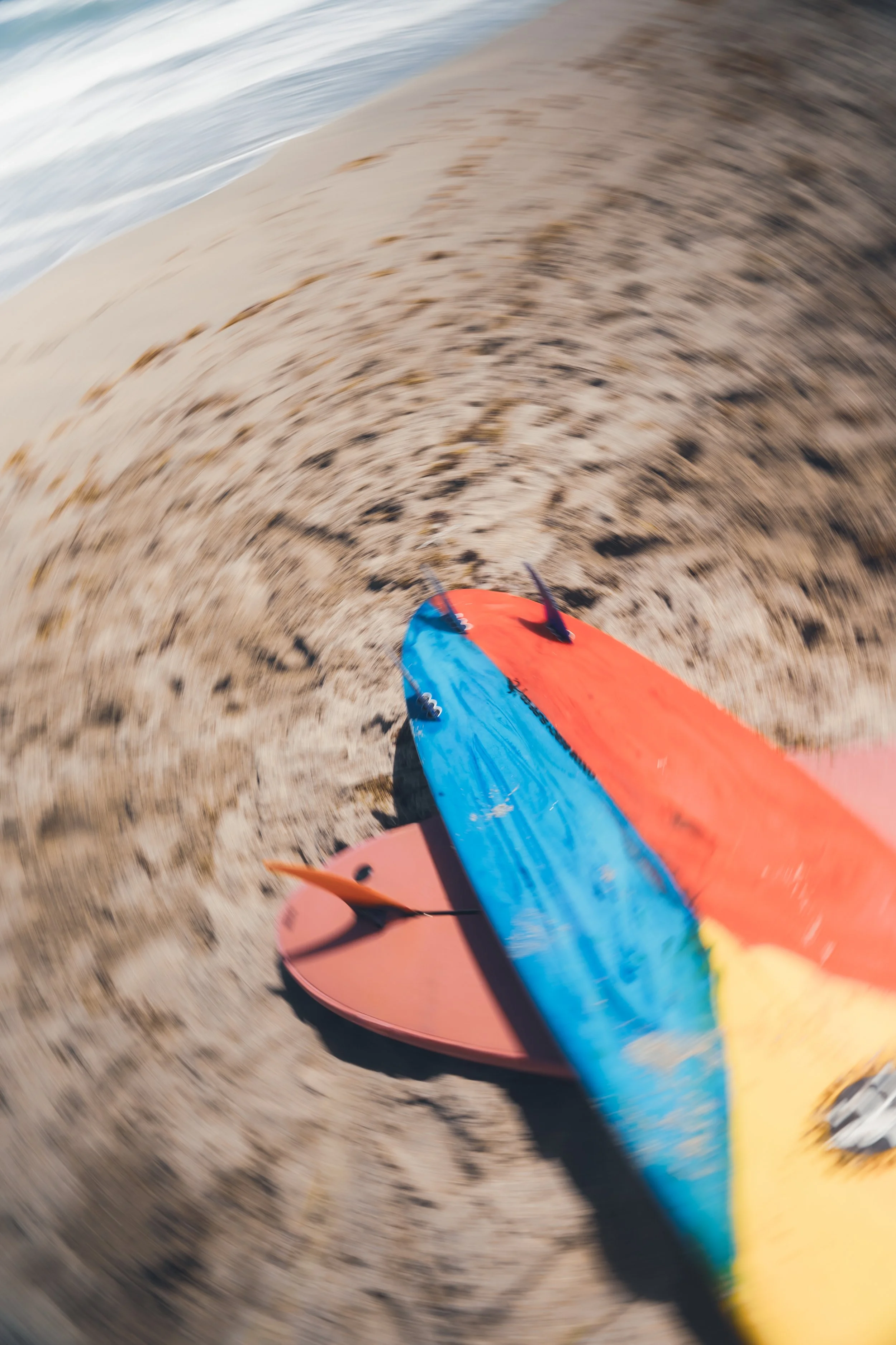 Colorful paddleboard on sandy beach with blurred background of ocean waves.