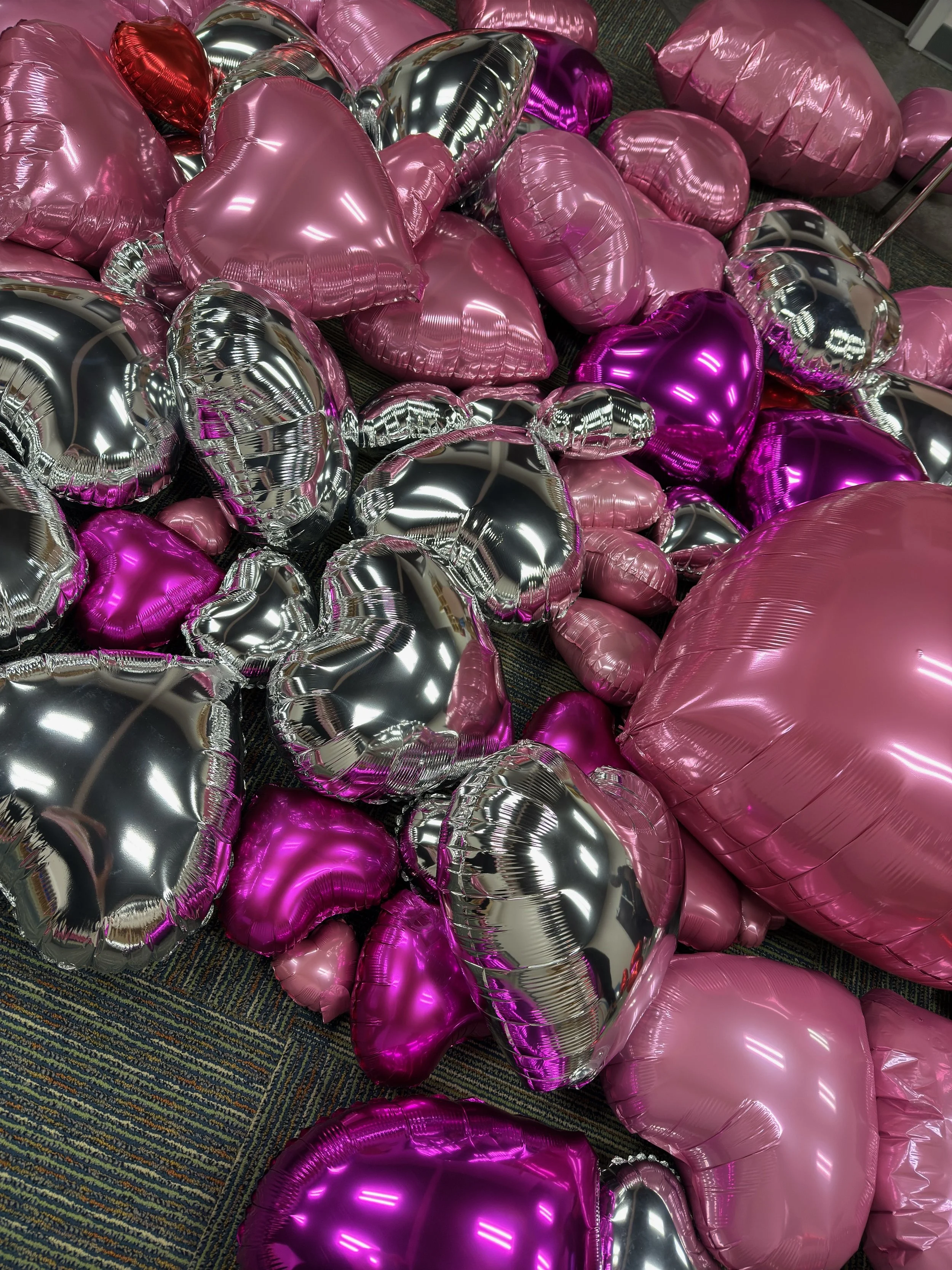 A large collection of heart-shaped balloons in pink, silver, purple, and red colors scattered on the floor.