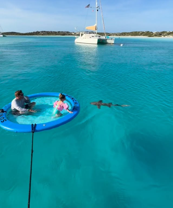 The Fine-A-Lee crew in a floating pool with a nurse shark, their catamaran behind them