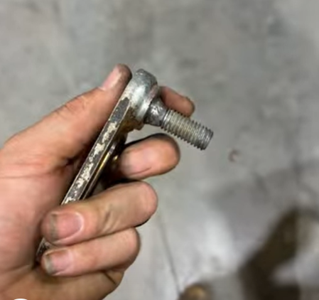 A person's hand holding a metal bolt with a long threaded shaft and a flat head of bolt that was machined.