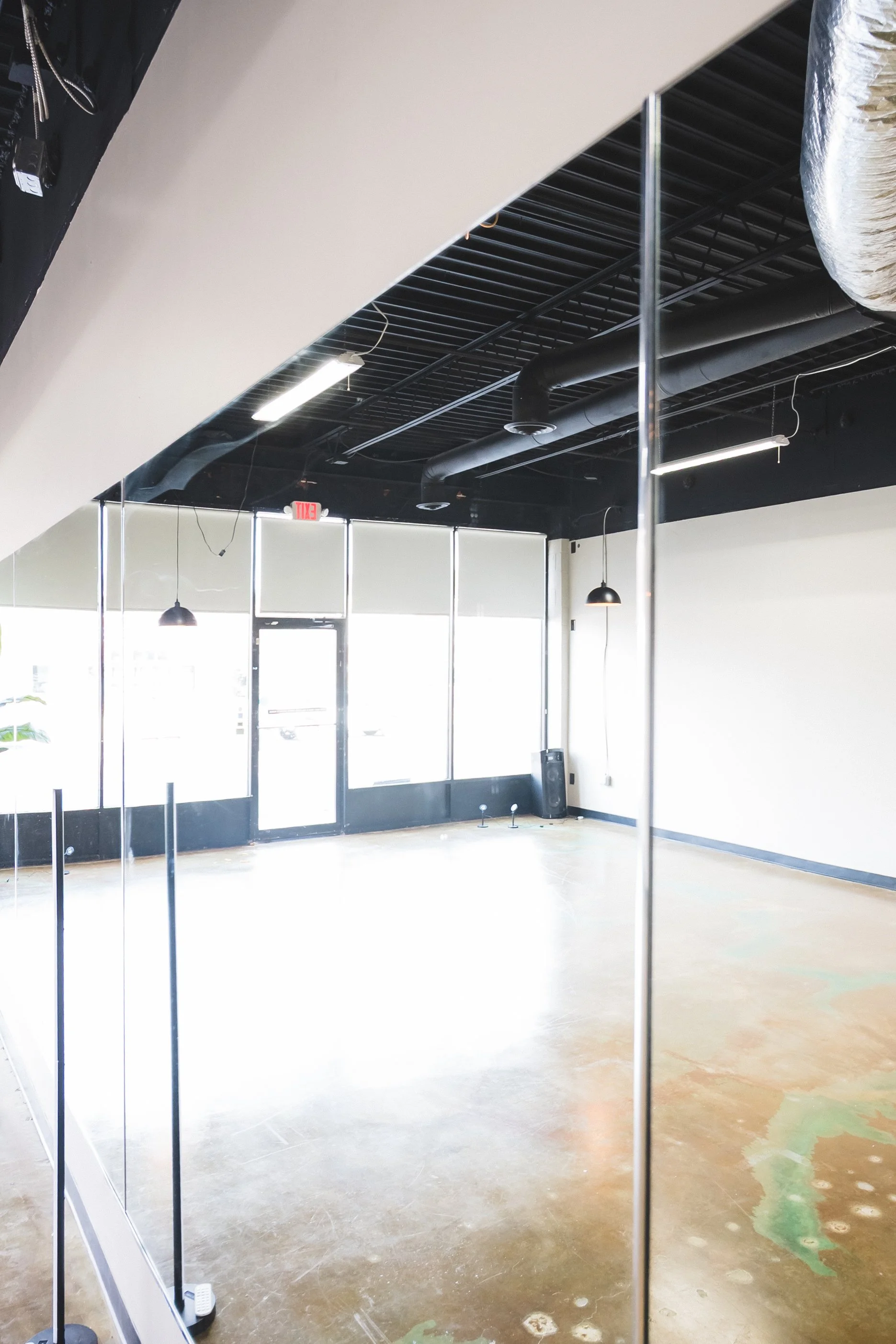 Empty commercial space with large windows, black ceiling with exposed pipes, and polished concrete floor.