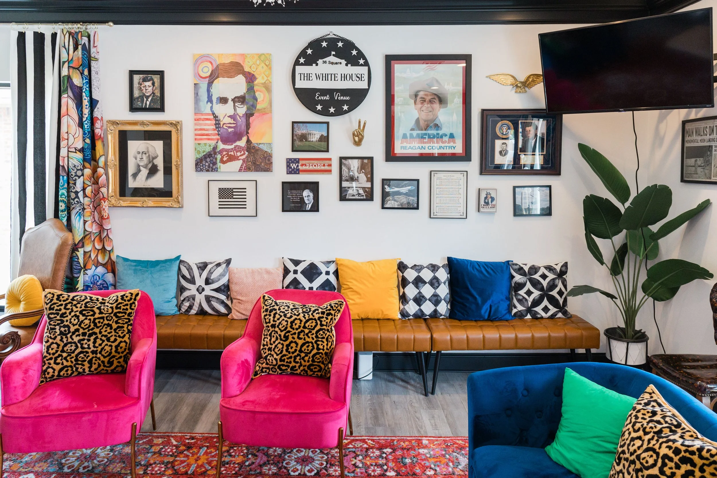Colorful living room with wall decorated with framed pictures, artwork, and memorabilia related to American politics, including images of Ronald Reagan and George Washington. The room features vibrant furniture including pink chairs with animal print