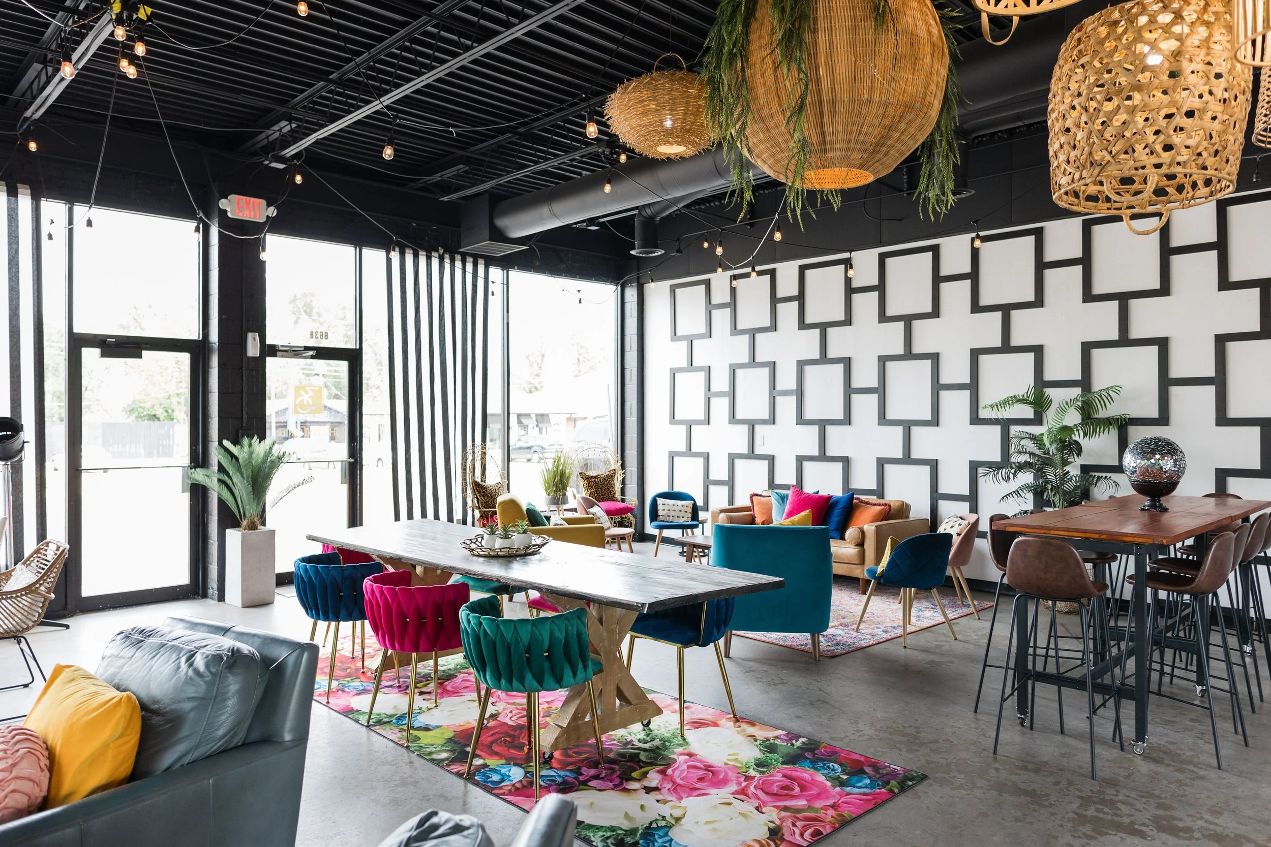 Bright, colorful interior of a modern lounge with various furniture, floral rugs, plants, and decorative hanging lights.