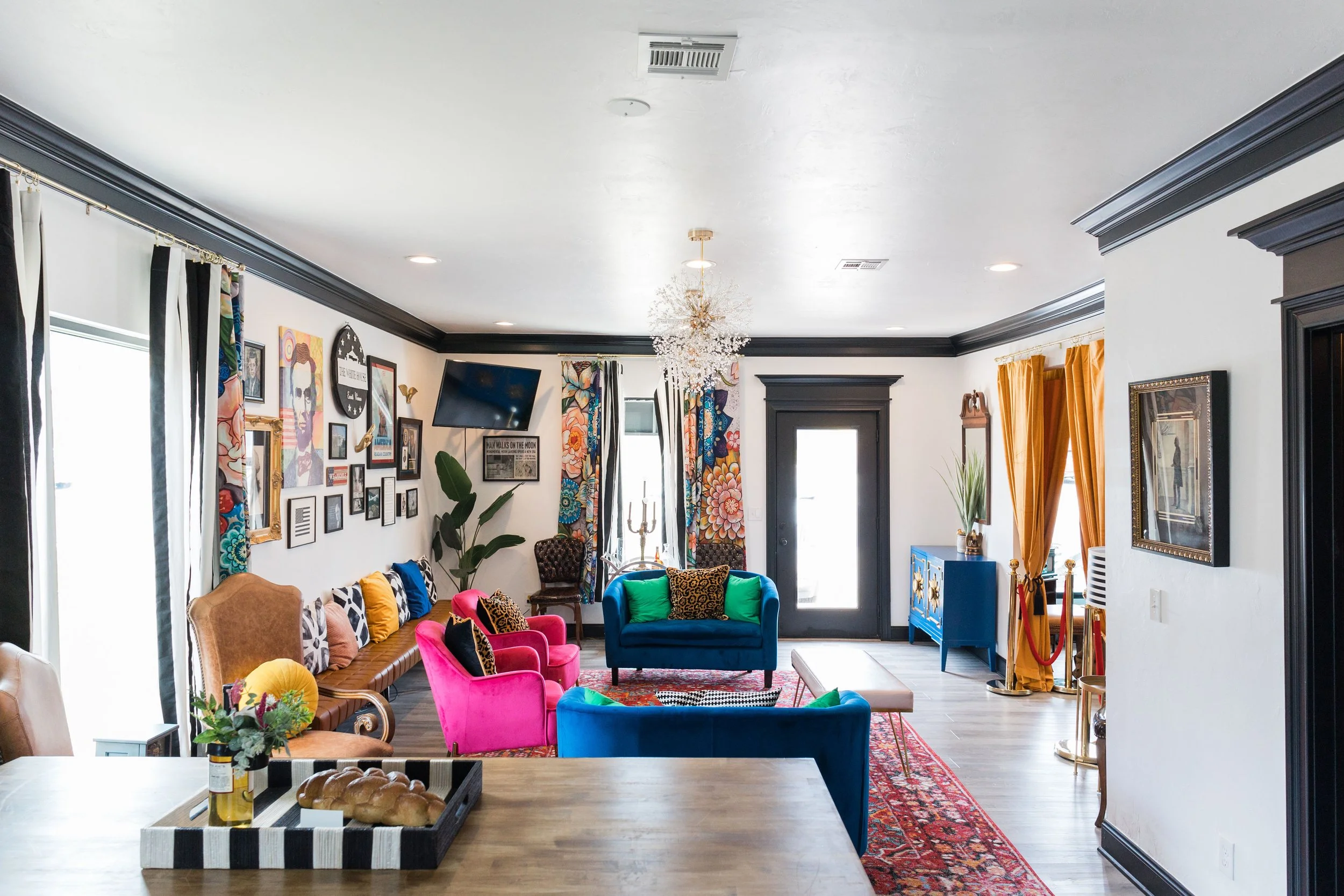 Colorful living room with various bright upholstered chairs, a gallery wall, colorful curtains, a chandelier, and a mix of vibrant decor.