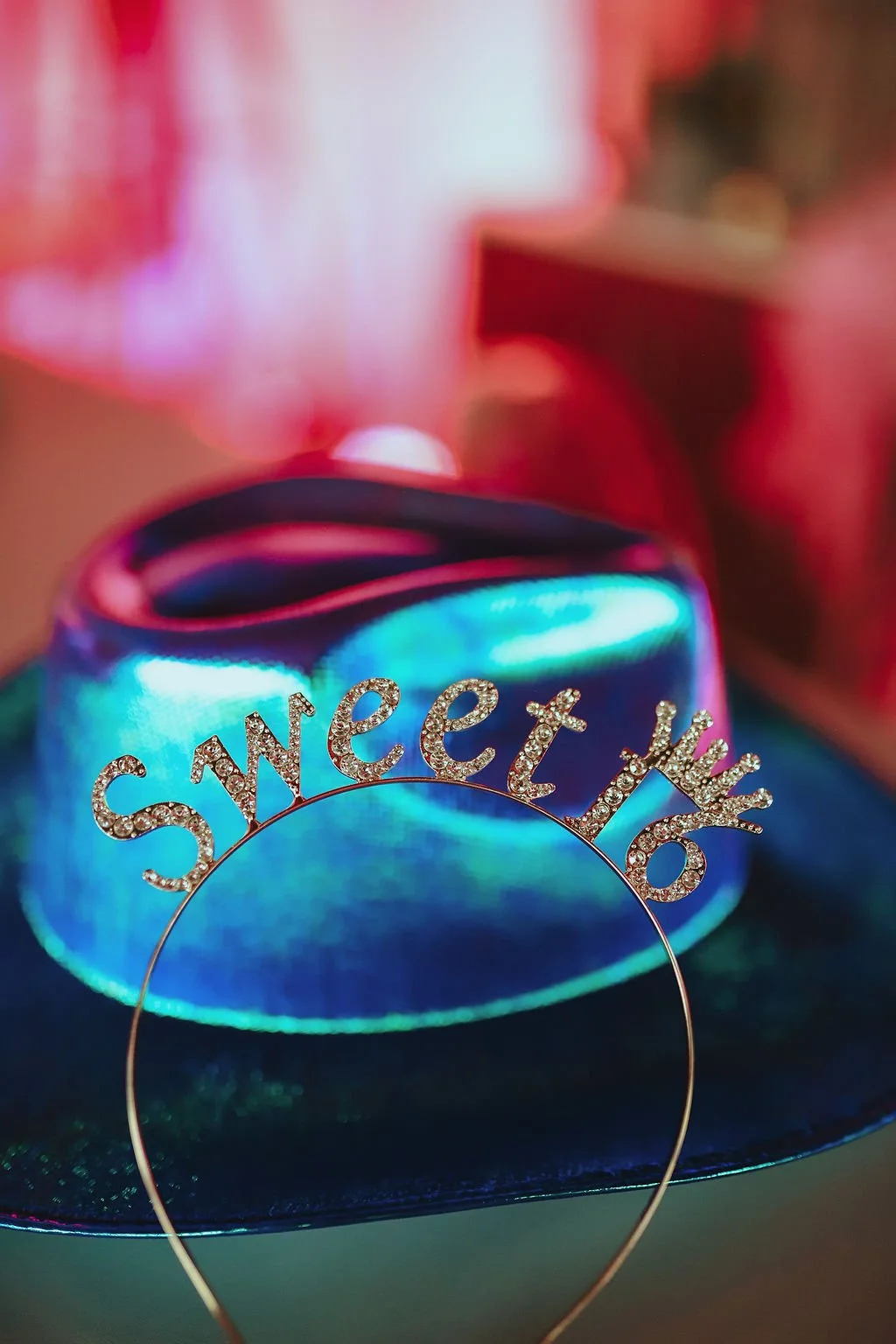A glittery headband that spells 'Sweetest' with rhinestones, set against a colorful, iridescent background.