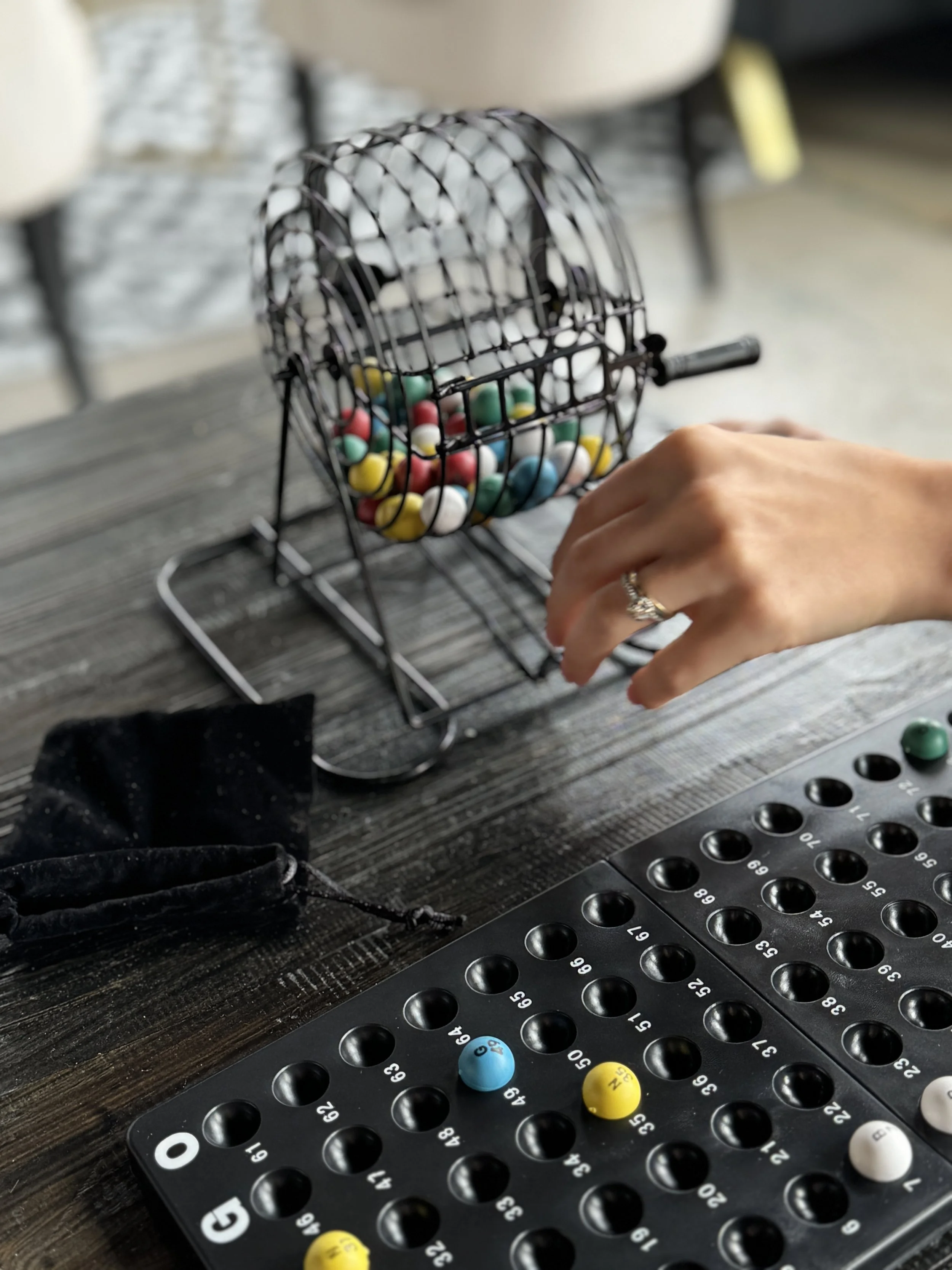 A hand is selecting a bingo ball from a cage containing colorful bingo balls. A bingo card with numbered holes and some balls on it is on the table.