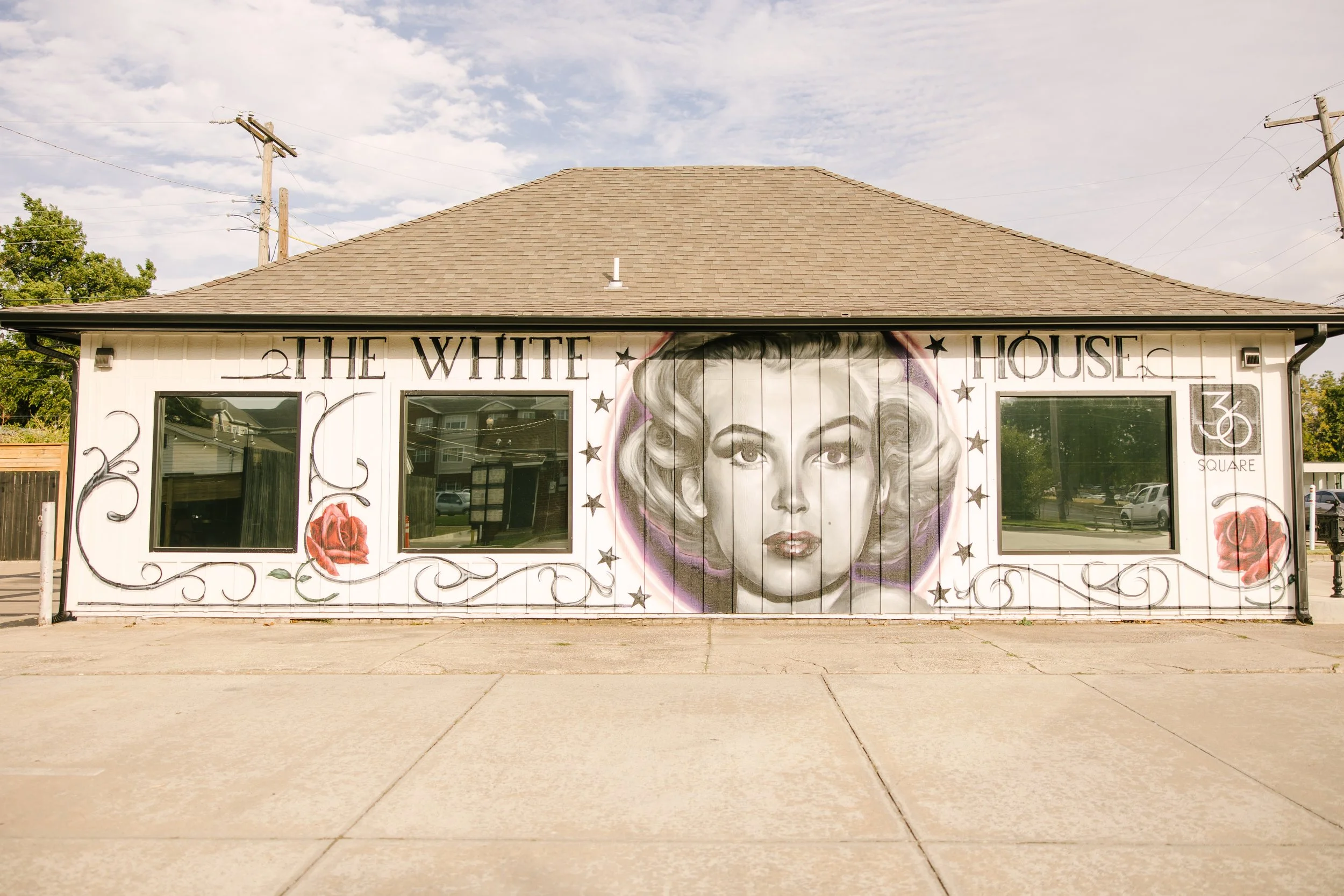 Building with mural of Marilyn Monroe's portrait, roses, and decorative lettering reading 'The White House, 3rd Square' on white walls.