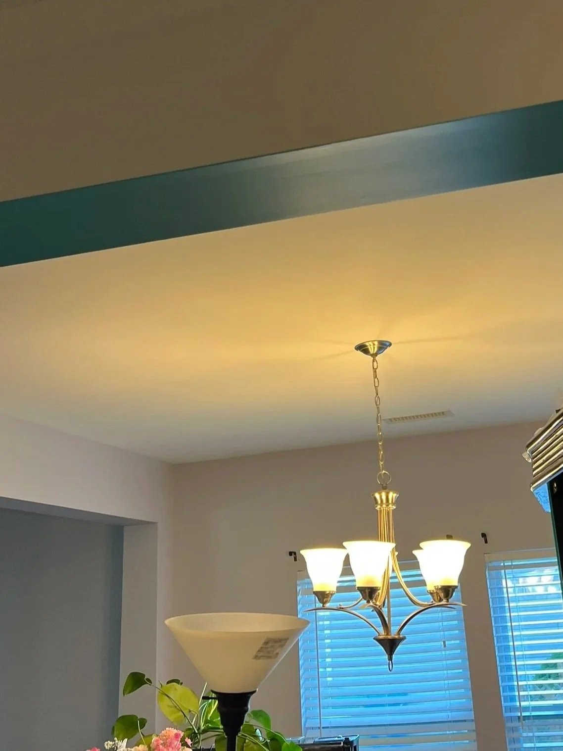 Interior view of a room with a ceiling chandelier, a wall-mounted lamp, and blue window blinds