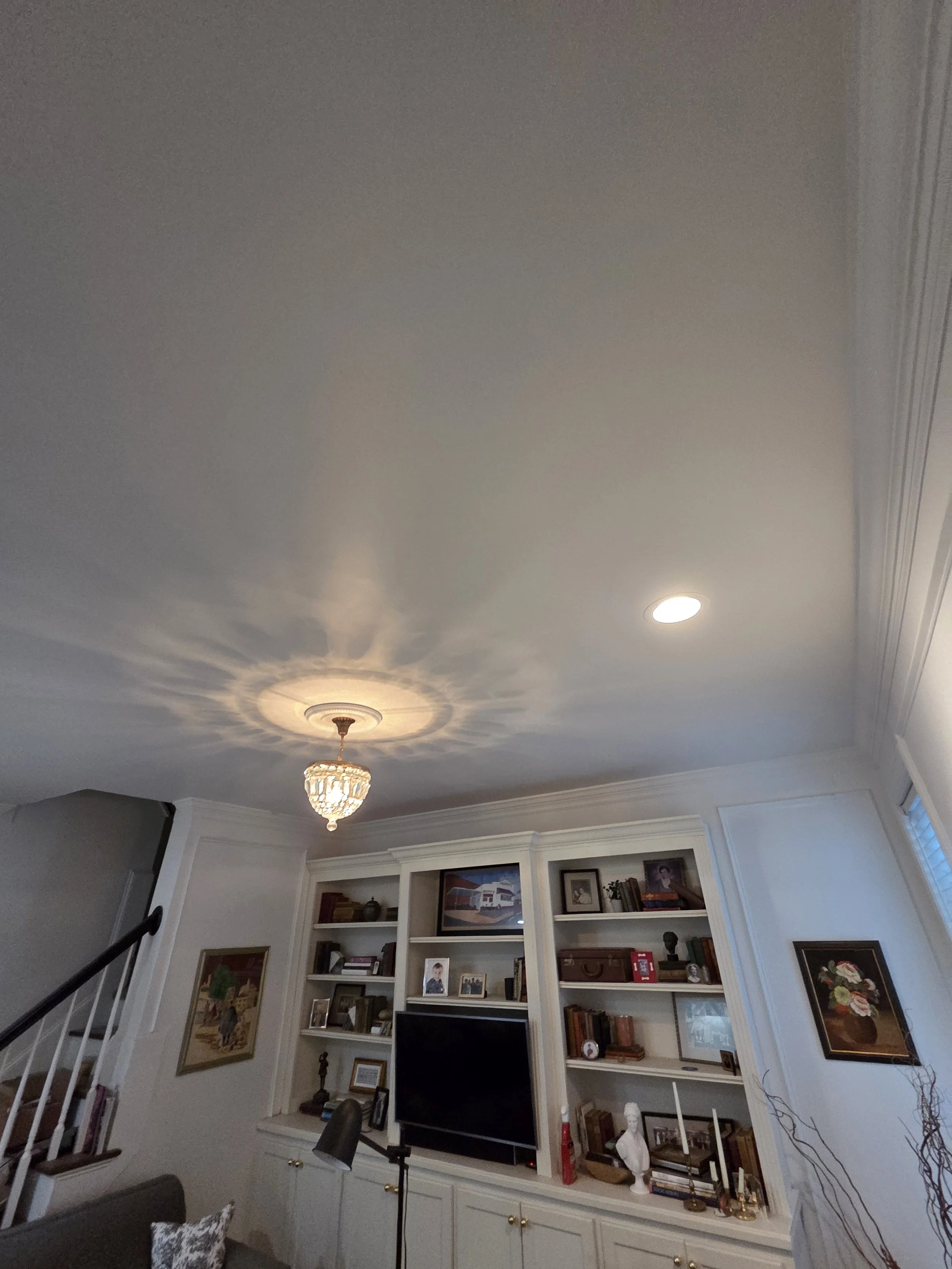 Living room with white built-in shelves, a large flat-screen TV, framed photos, decorative items, a chandelier, and a ceiling light fixture.