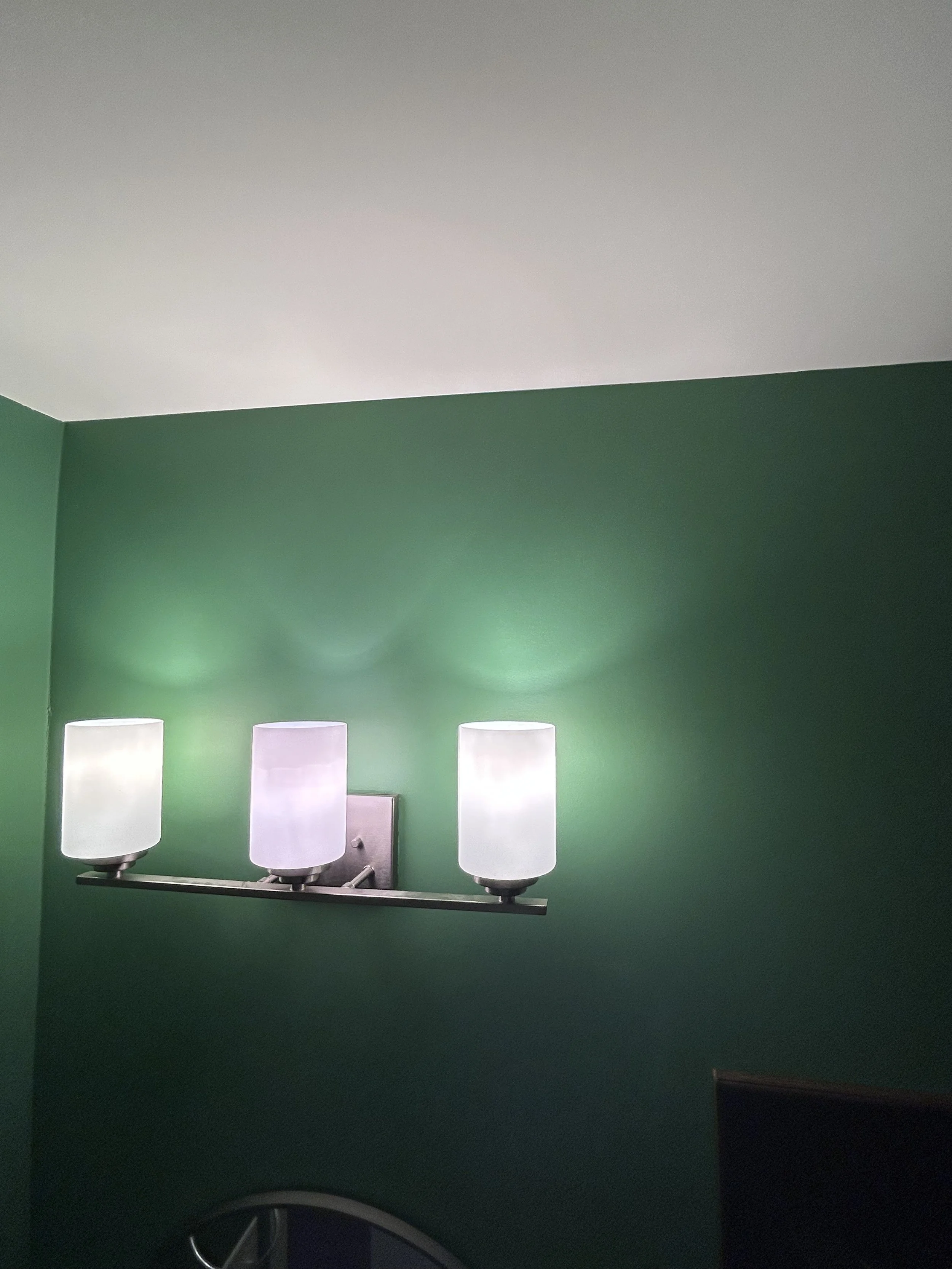 Green wall with a three-light bathroom vanity fixture with white shades.