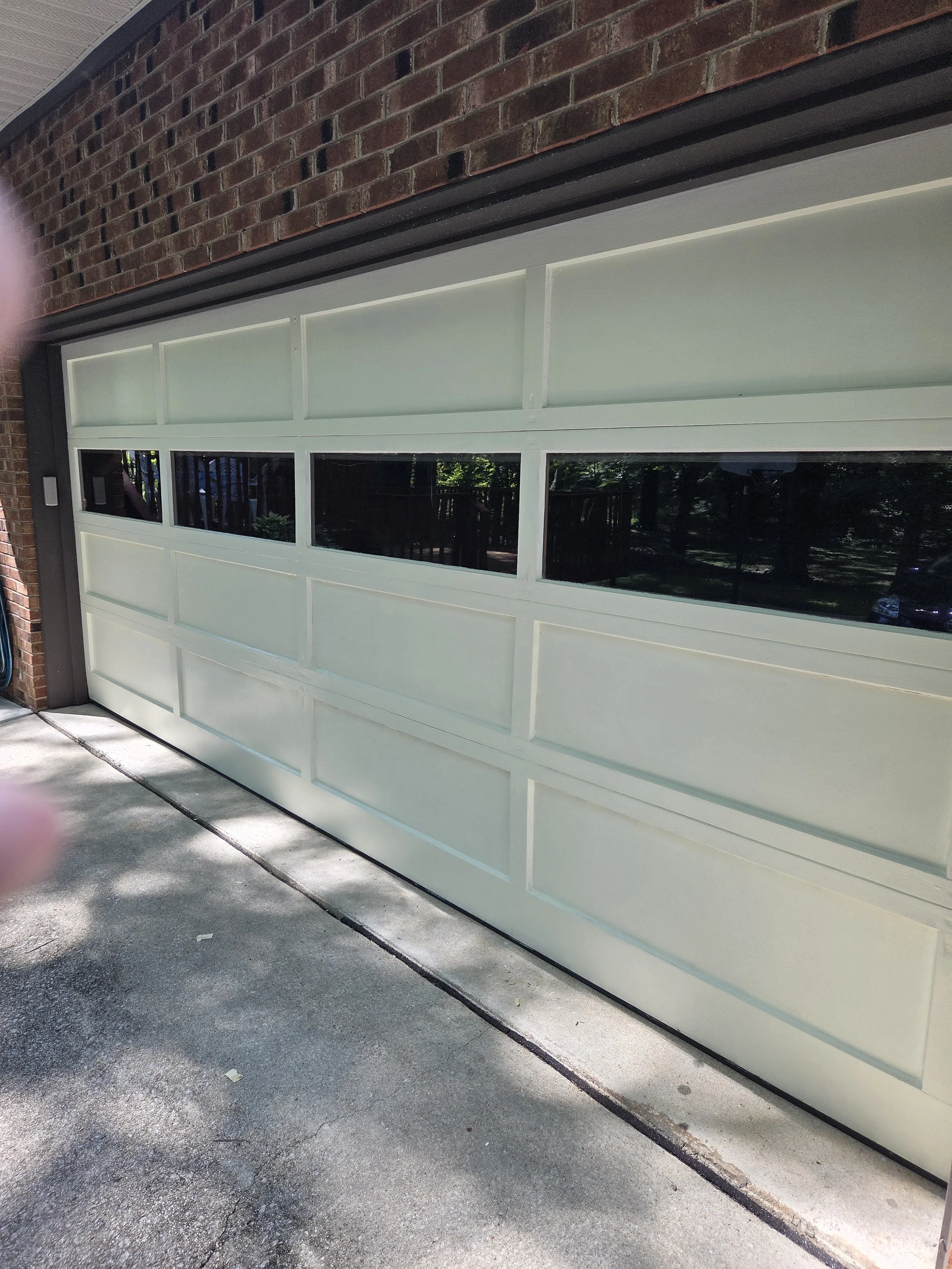 Closed cream-colored garage door with glass panels, set against a brick wall, with a concrete driveway in front.