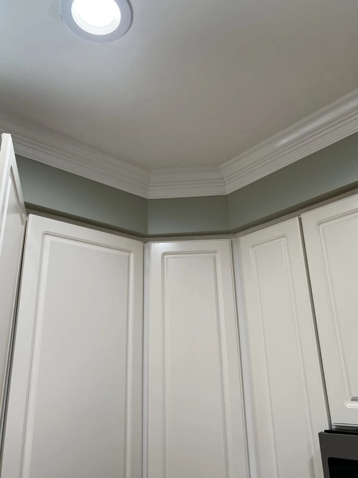 Kitchen corner with white cabinets, crown molding, green walls, and a ceiling with a recessed light.