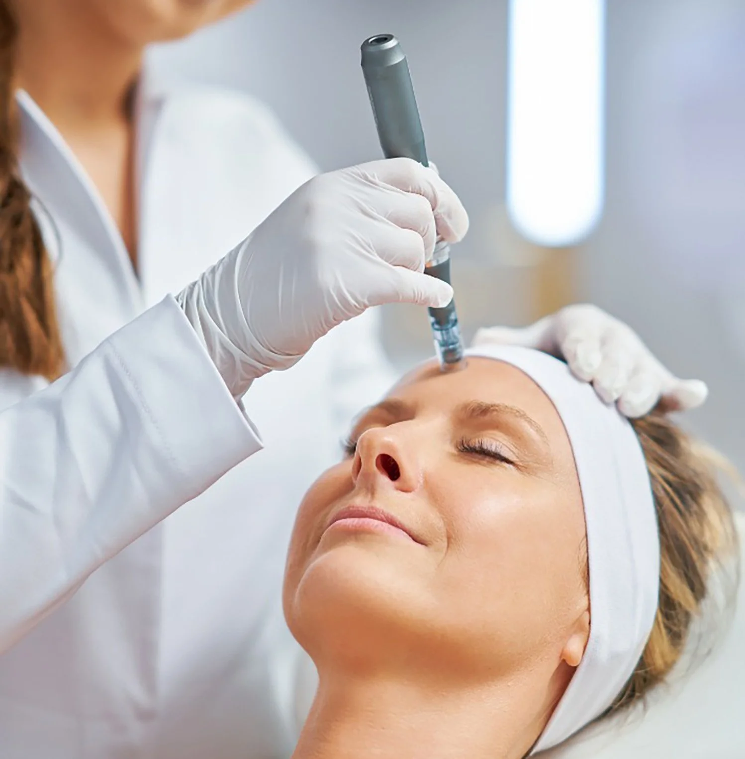 A woman receiving a cosmetic injection in her forehead from a healthcare professional wearing gloves.