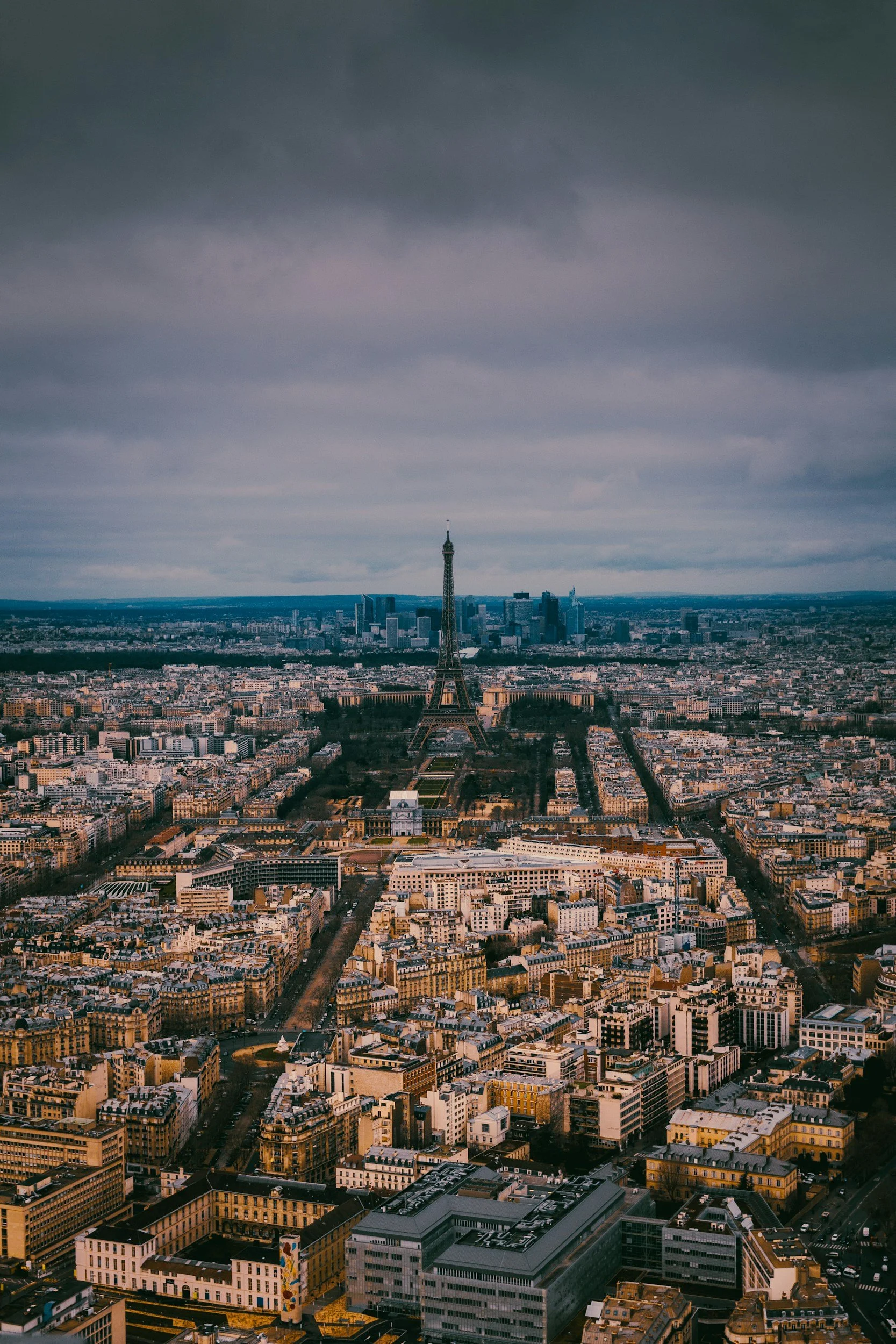 Vue aérienne de Paris avec la tour Eiffel au centre, bâtiments résidentiels et commerciaux, ciel nuageux.