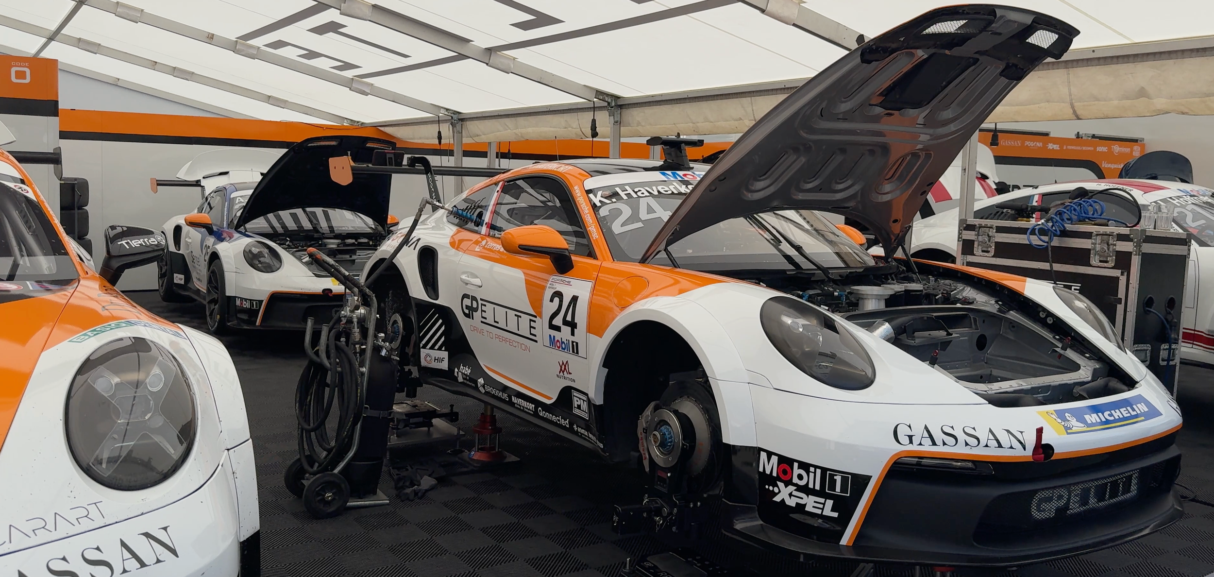 Race cars in a garage with open hoods and wheels removed, showing mechanical parts and setups for racing.