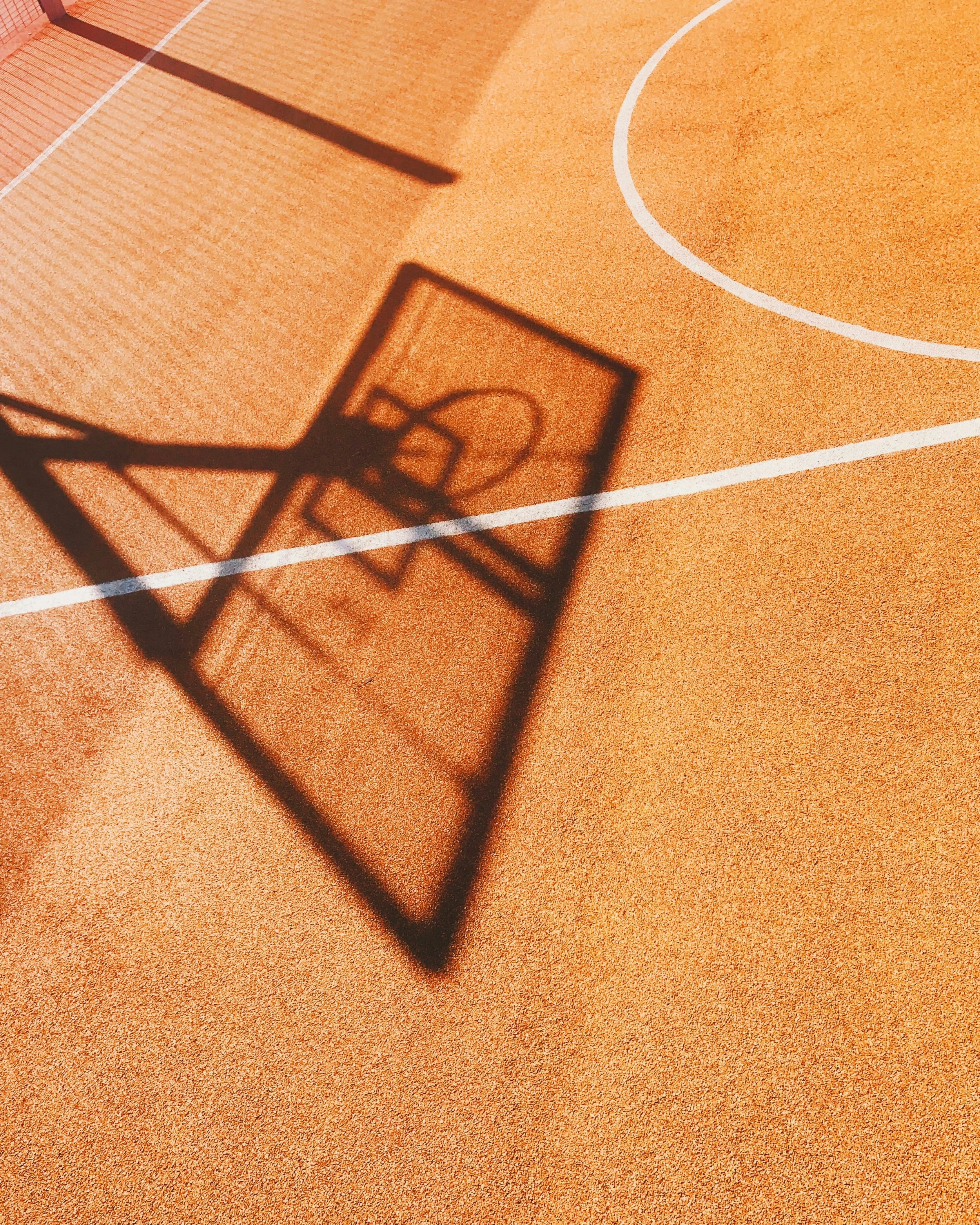 Shadow of a basketball hoop cast on an indoor basketball court with orange surface and white court lines.