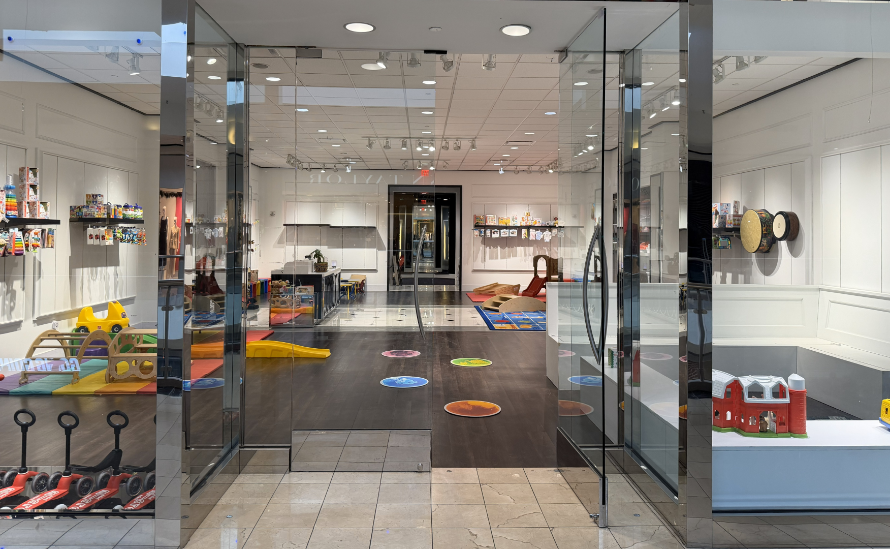 A white bookshelf filled with children's toys, books, and stuffed animals. The top shelf has toys and stuffed animals in see-through bags. The middle shelf displays children's books, stuffed dolls, and toys. The lower shelves contain more toys, plush animals, and colorful balls.