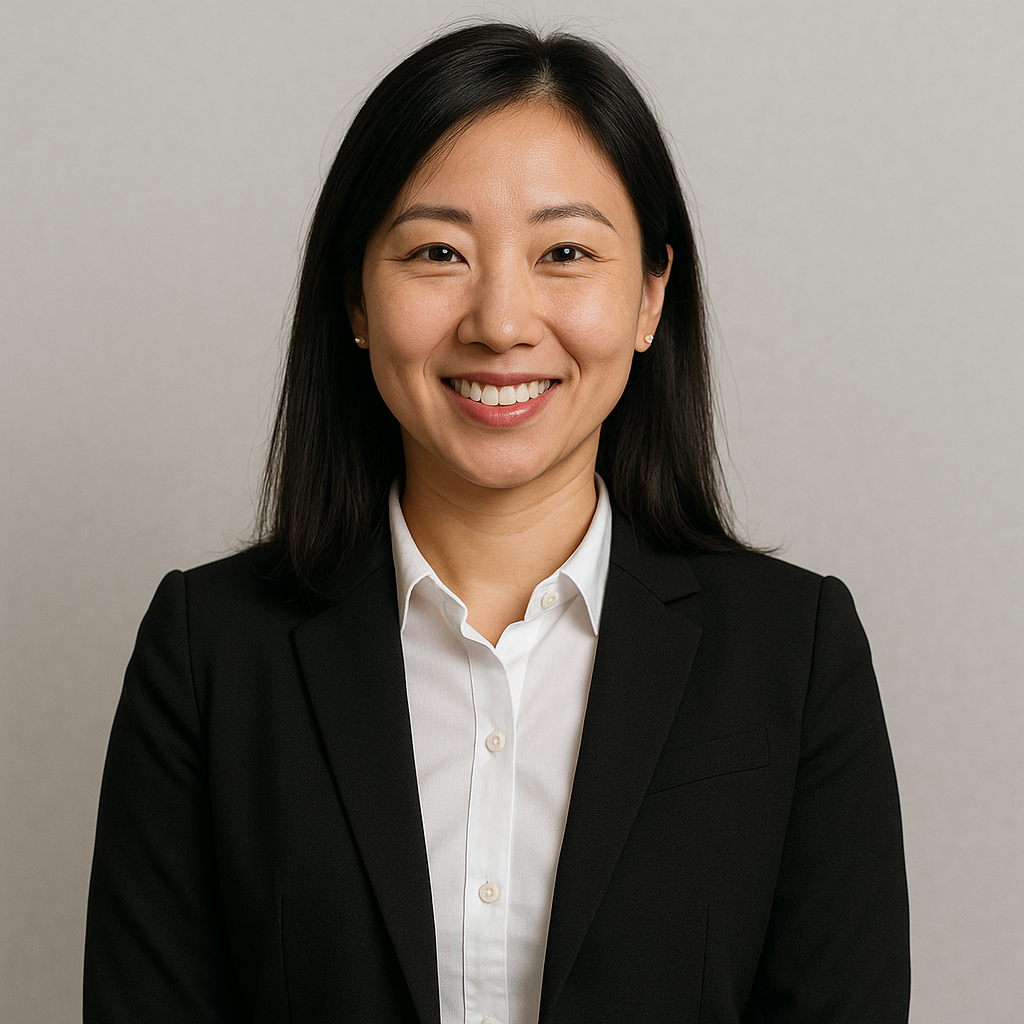 A professional woman smiling, wearing a black blazer and white blouse, against a plain light gray background.